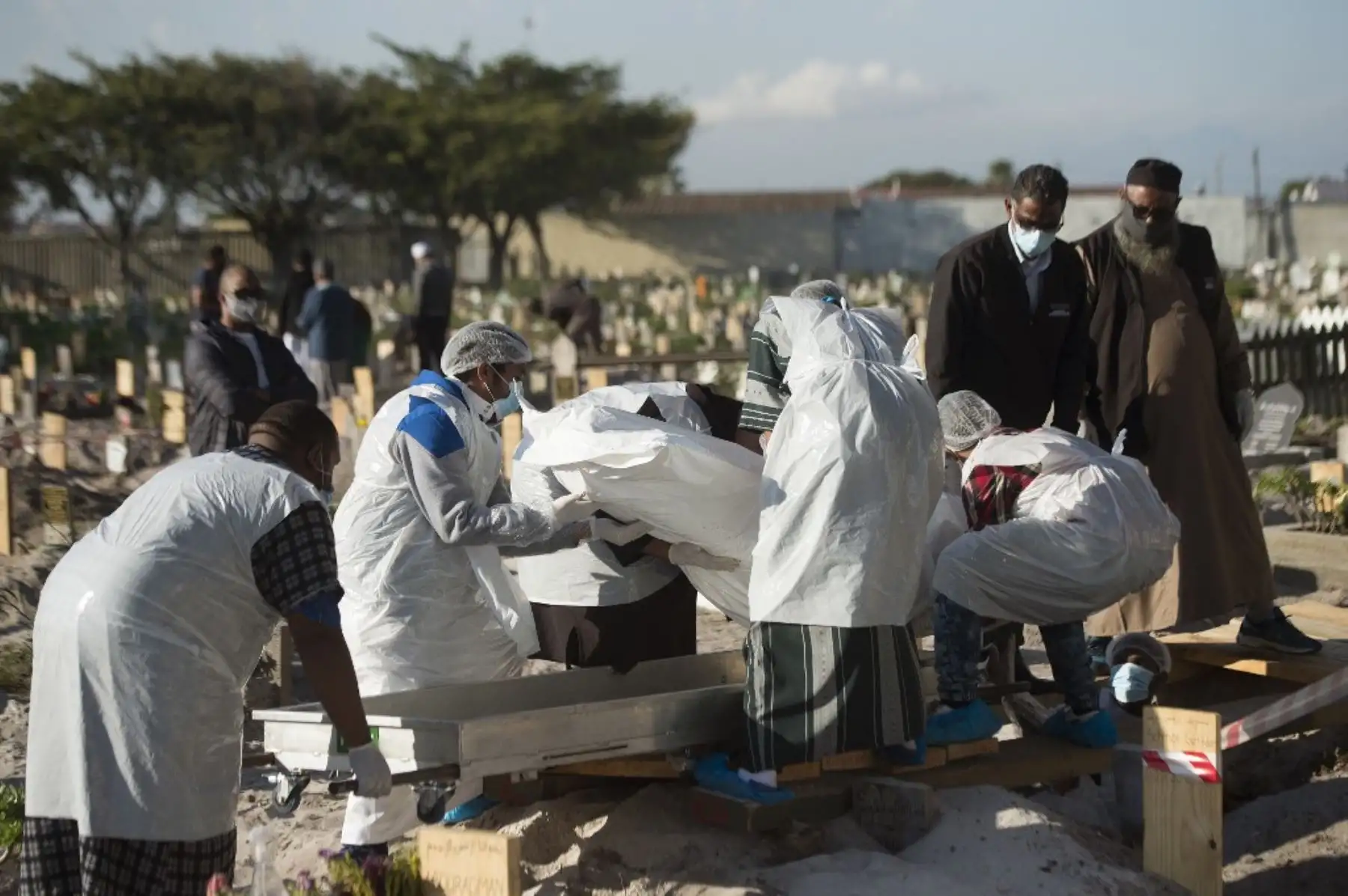 Miembros de una familia vestidos con equipo de bioseguridad colocan el cuerpo de un hombre musulmán que murió de coronavirus, en el cementerio de Klip Road, Grassy Park, Ciudad del Cabo. Foto: AFP