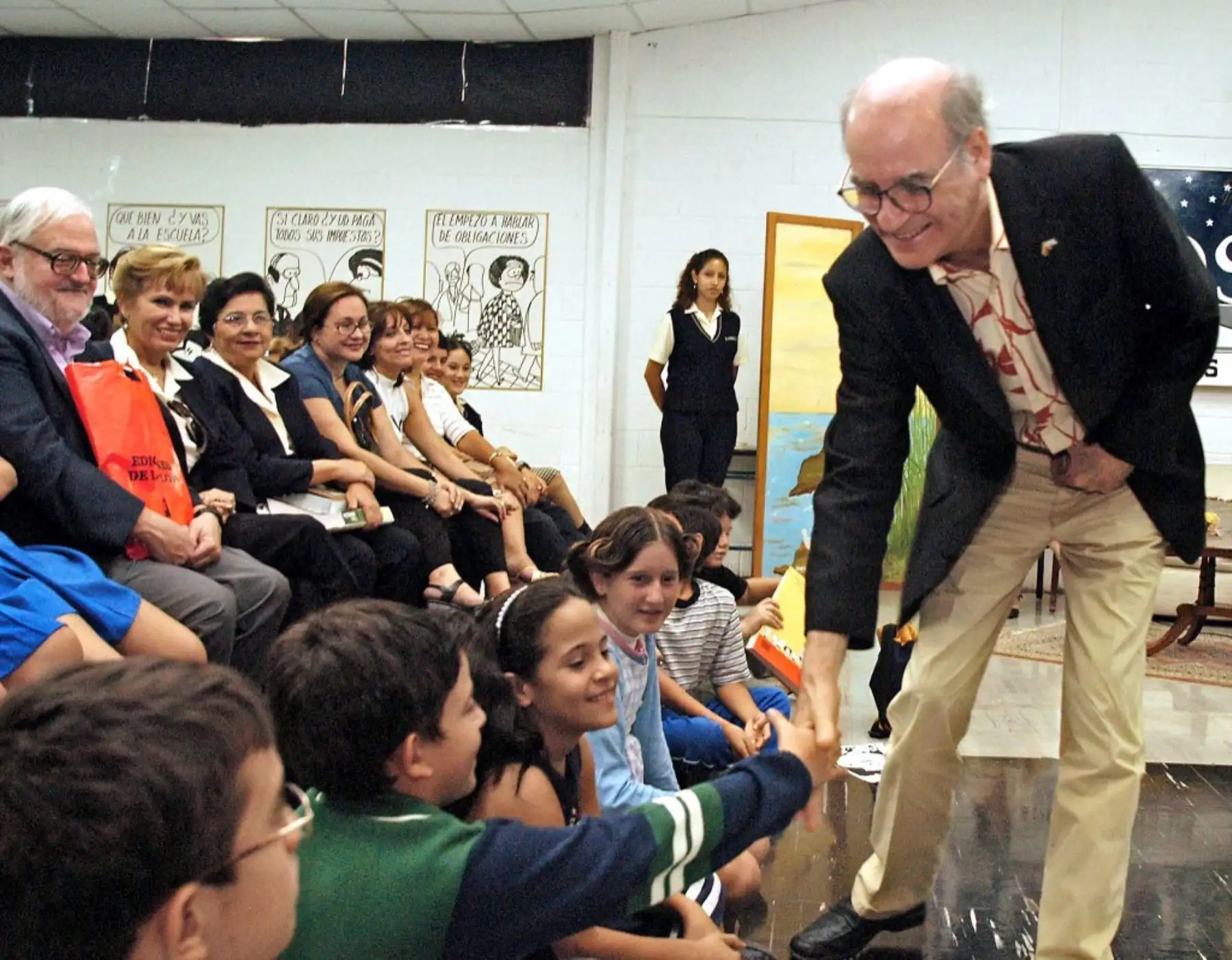El dibujante de historietas, Joaquín Salvador Lavado, conocido como Quino, saluda a unos niños al empezar una charla en Guayaquil, Ecuador, el 21 de agosto de 2003. Quino, creador de "Mafalda", realizaba giras para dictar en diferentes colegios. Foto: AFP