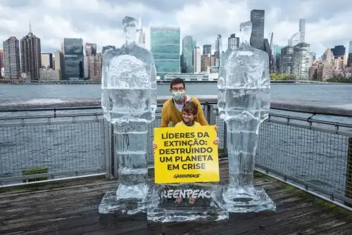Fotografía cedida por Greenpeace donde aparece un hombre y su hijo mientras sostienen un cartel en portugués que dice "Rostros de la extinción: alimentando un planeta en crisis" junto a dos esculturas de hielo de tamaño natural de los presidentes de Estados Unidos, Donald Trump (i), y de Brasil, Jair Bolsonaro (d), hoy en un pequeño muelle frente al edificio de la ONU en Nueva York (EE.UU.). Foto: EFE