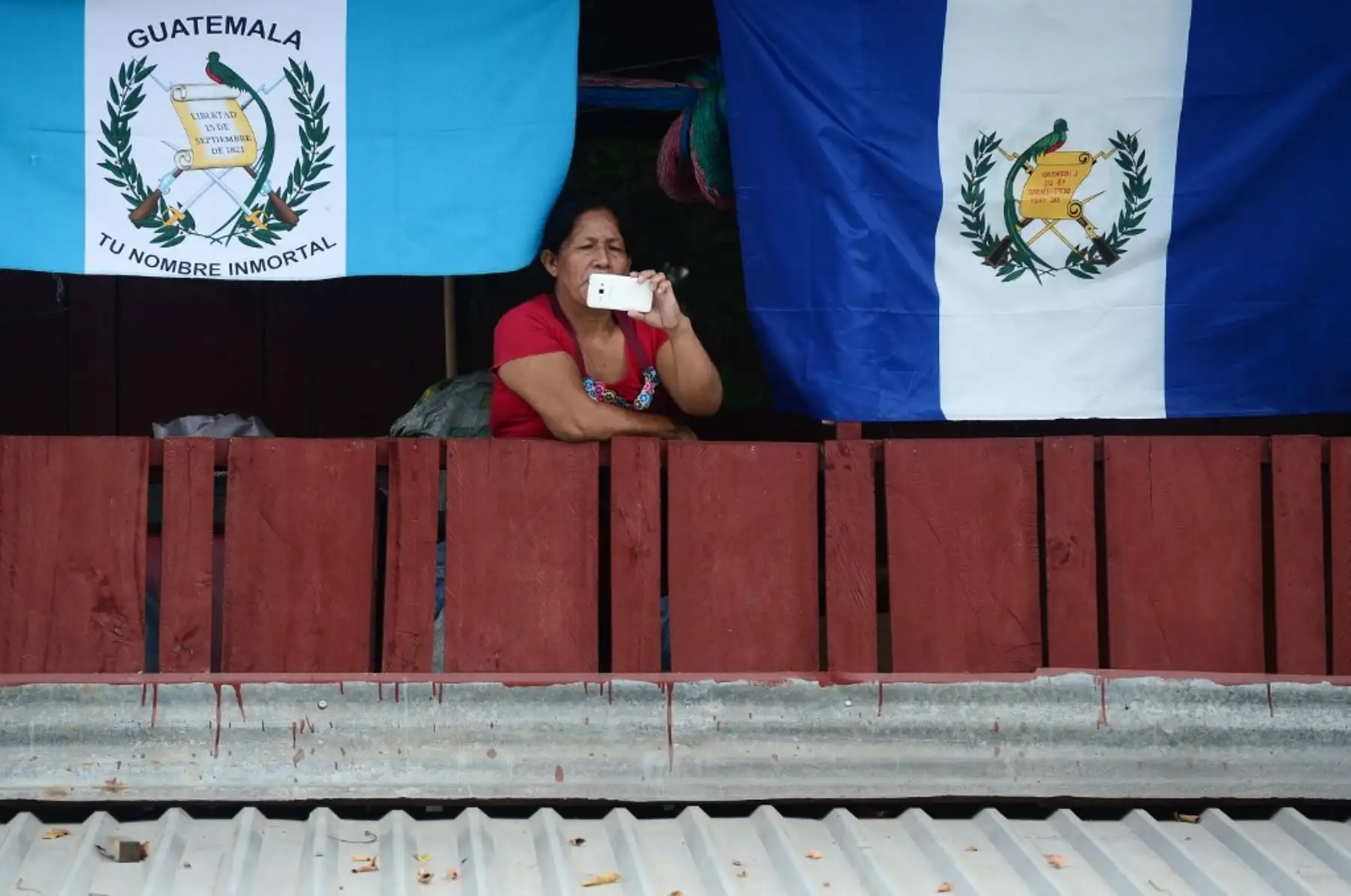 Una mujer bajo banderas guatemaltecas y hondureñas, registra como migrantes hondureños rompen la valla policial para ingresar a Guatemala en su camino a los Estados Unidos, en la frontera de Corinto, Honduras. Foto: AFP