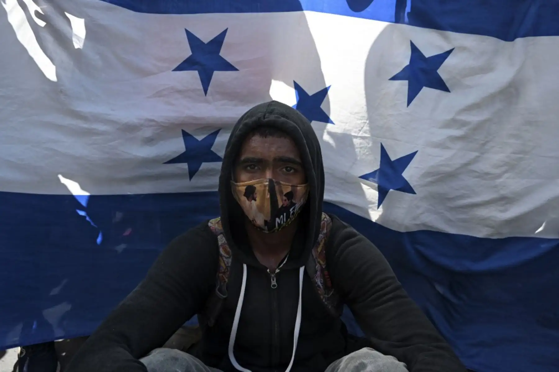 Un migrante hondureño se sienta frente a una bandera hondureña en Entre Ríos, Guatemala, luego de cruzar la frontera de Honduras en su camino a los Estados Unidos en una caravana. Foto: AFP