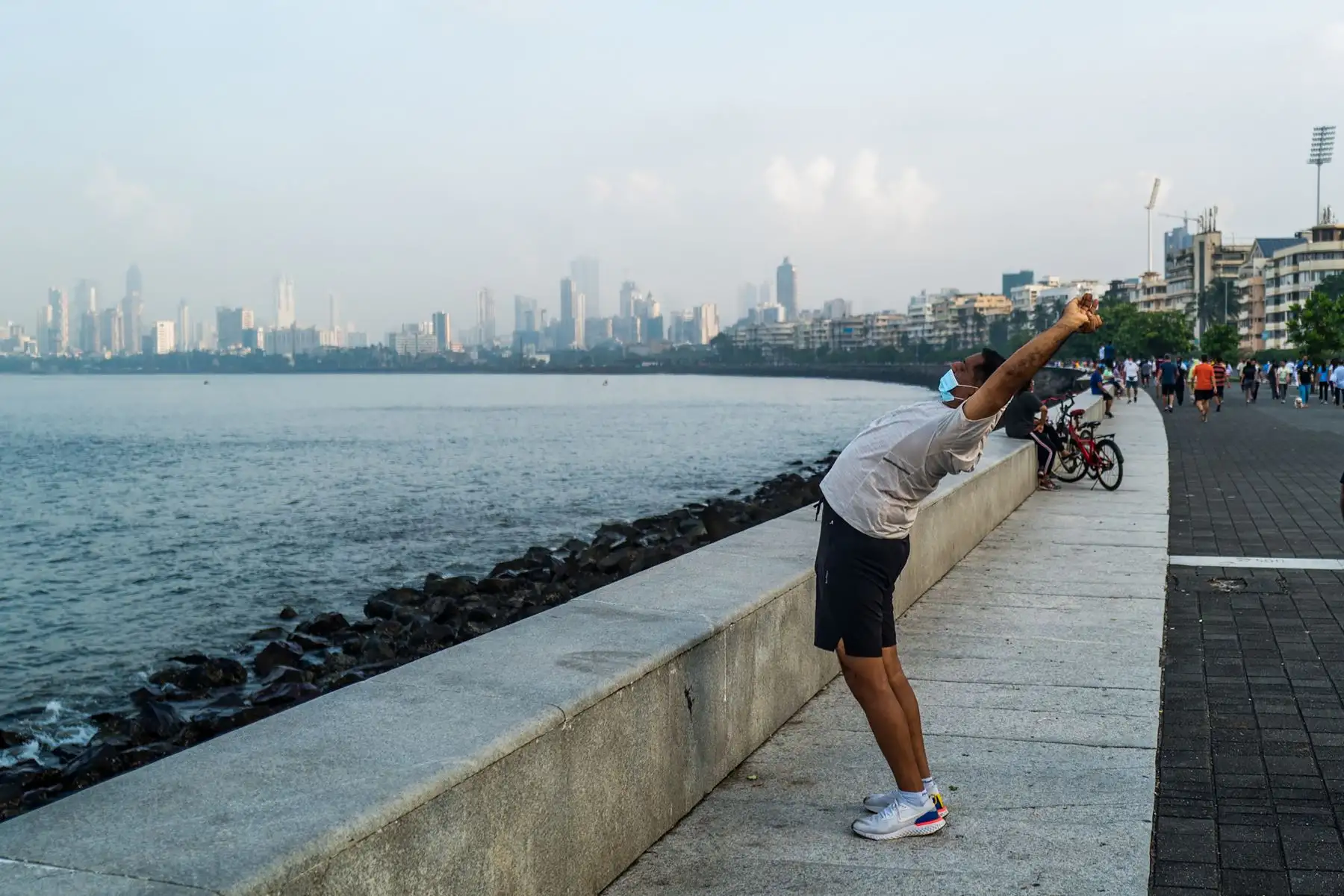 Un hombre que lleva una mascarilla como medida preventiva contra el coronavirus realiza estiramientos en el paseo marítimo de Marine Drive, en Mumbai. Foto: AFP