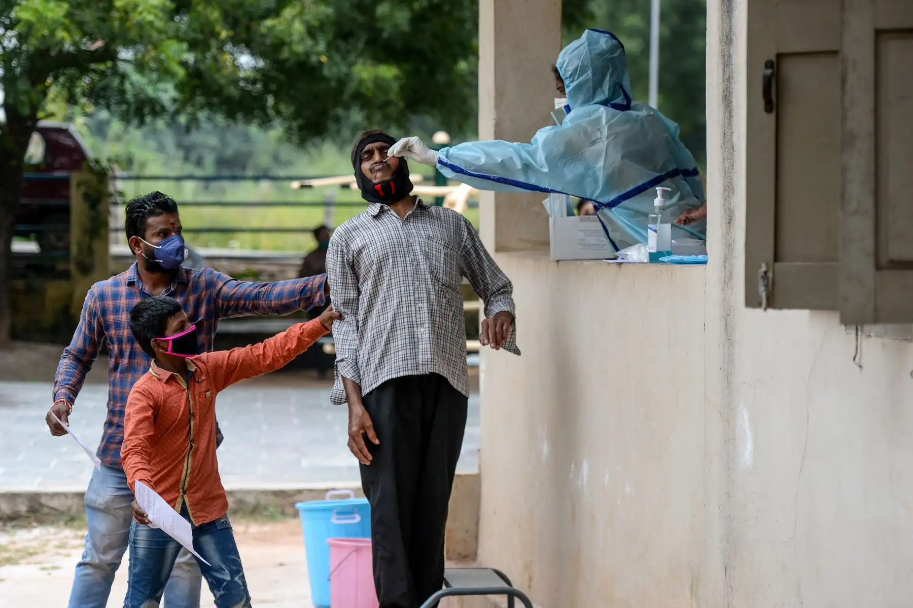 Los residentes sostienen a un hombre mientras un trabajador de la salud toma una muestra de hisopo para detectar el coronavirus, en un centro de gimnasio comunitario en las afueras de Hyderabad. Foto: AFP
