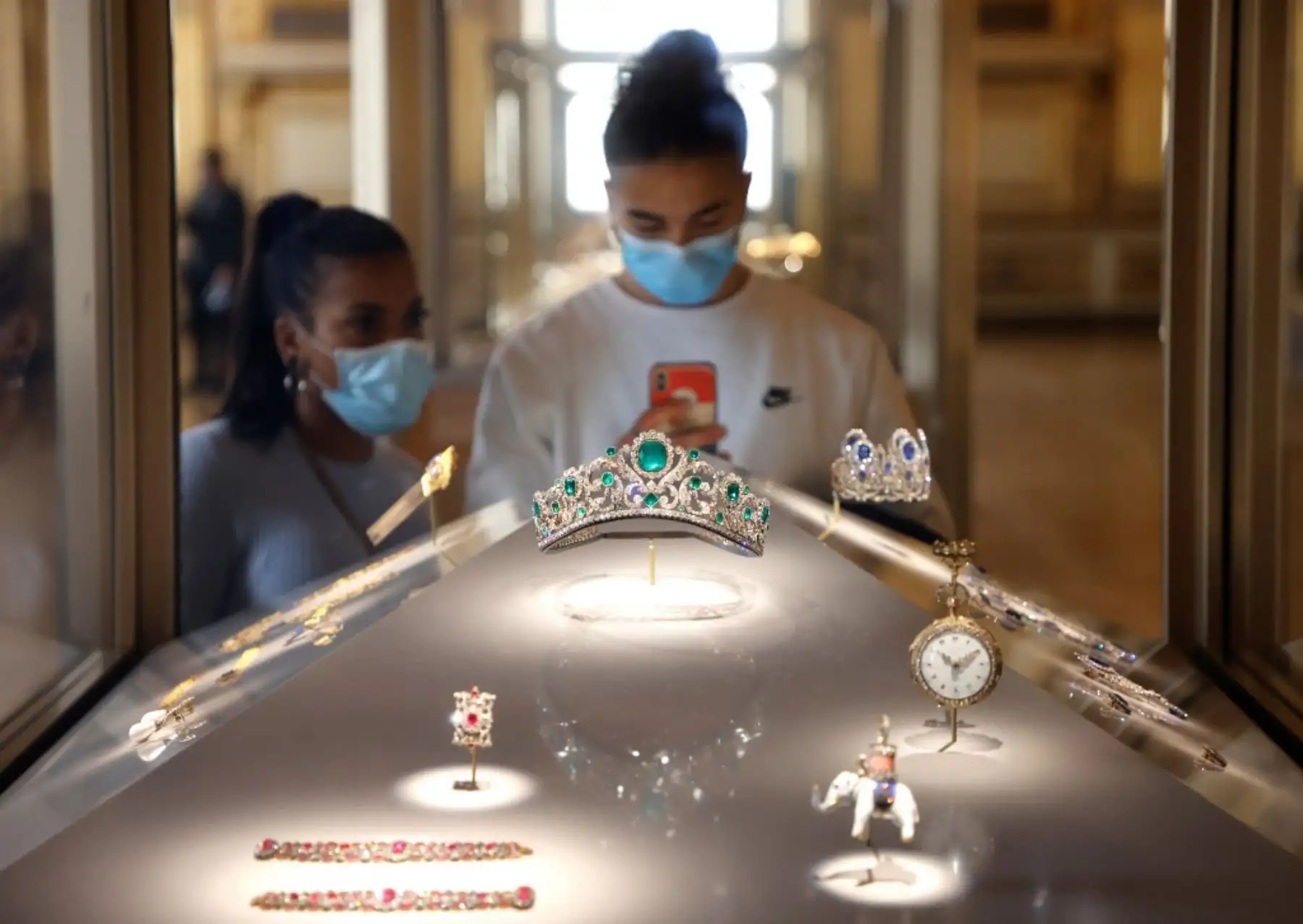 Visitantes con mascarillas miran la Diadema de la Duquesa de Angulema expuesta en una ventana que se exhibe en la galería Apolo del Museo del Louvre, abandonada por los turistas debido a la pandemia de Covid-19, en París. Foto: AFP