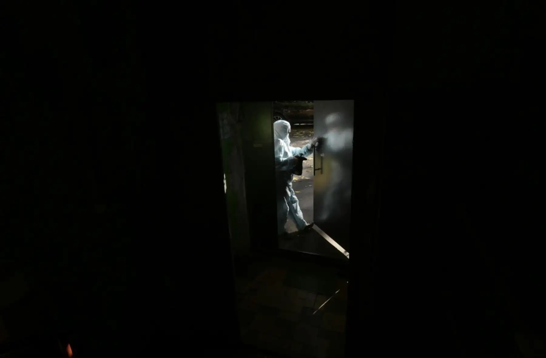 Un trabajador comunal con equipo de protección personal (EPP) rocía desinfectante en la puerta de un edificio residencial en Moscú. Foto: AFP