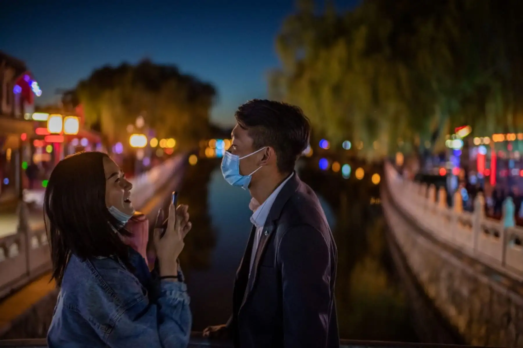 Una pareja que usa máscaras faciales como medida preventiva contra el Covid-19 se ríe mientras se toman fotos con un teléfono en un puente en el lago Hu Hai en Beijing. Foto: AFP