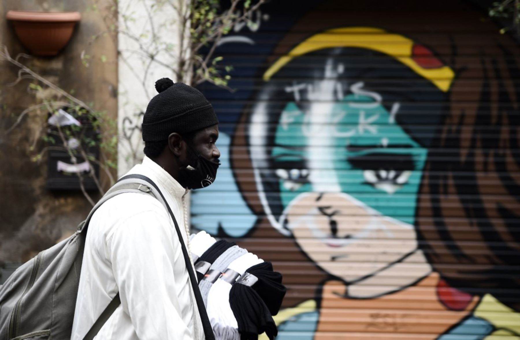 Un vendedor ambulante, con una mascarilla, camina frente a un mural en el centro de Roma. Foto: AFP
