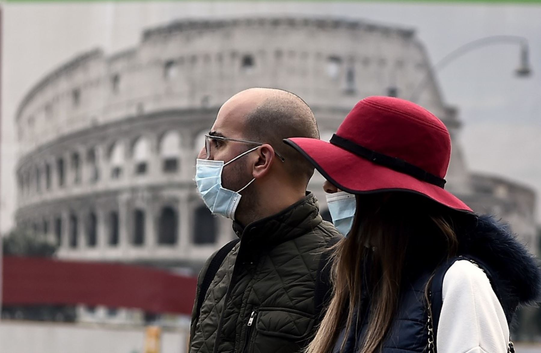 Una pareja con mascarillas pasa junto a un cartel que representa el Coliseo en medio de la pandemia de Covid-19 en el centro de Roma. Foto: AFP