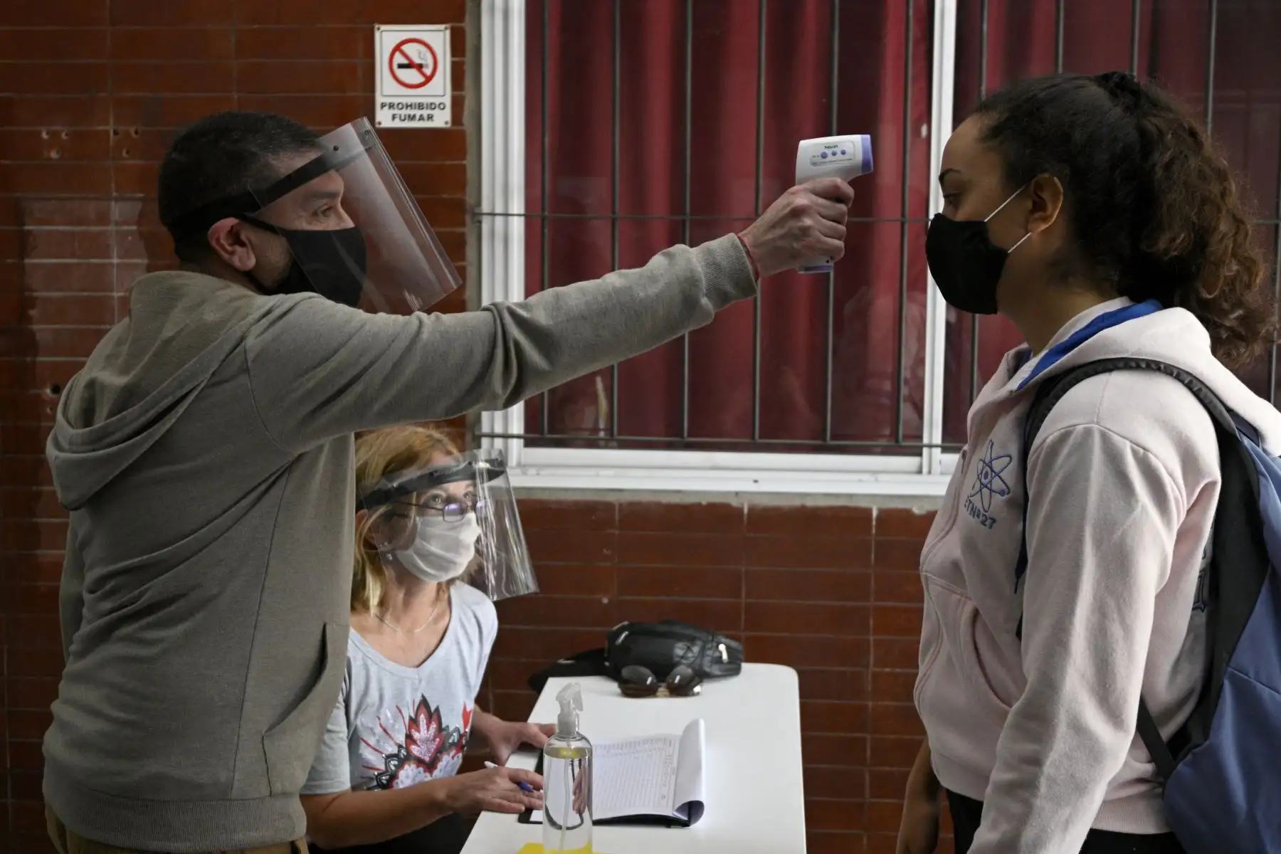 Los trabajadores de una escuela secundaria de Buenos Aires le controlan la temperatura a una estudiante antes de que ingrese sus clases. Foto: AFP