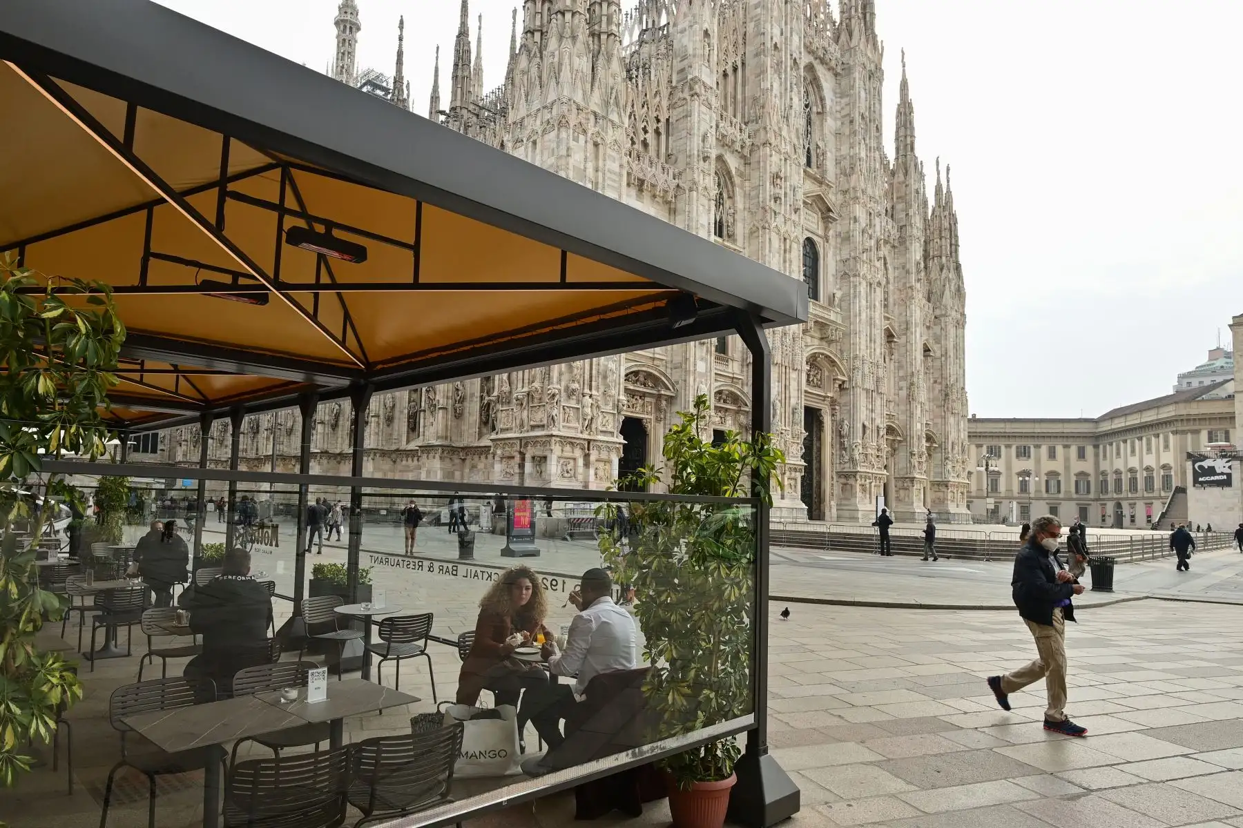 Personas con mascarillas transitan por la Catedral de Milán mientras algunos visitan restaurantes en medio del rebrote por coronavirus. Foto: AFP