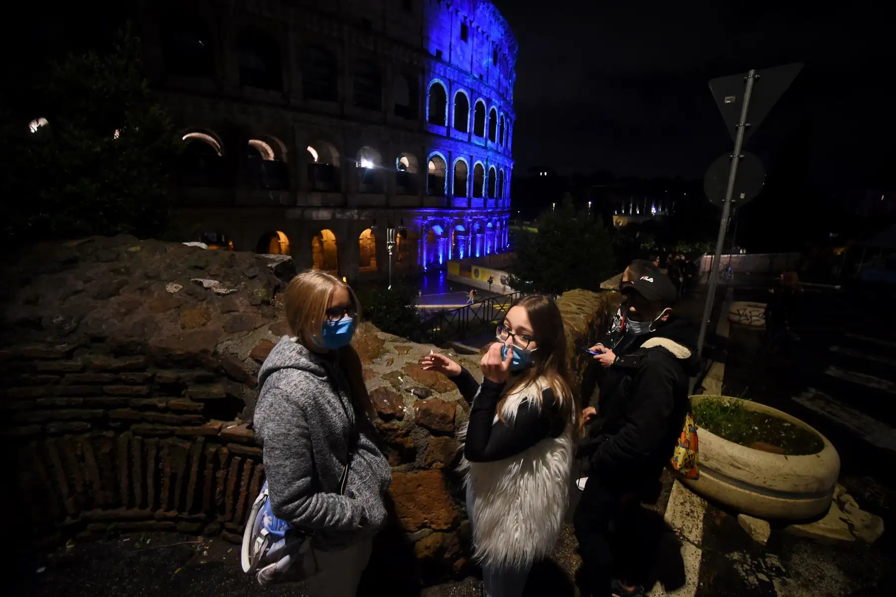 Las personas que llevan máscaras faciales dialogan junto al coliseo que se ilumina por el 75 aniversario de la FAO, en el centro de Roma. Foto: AFP