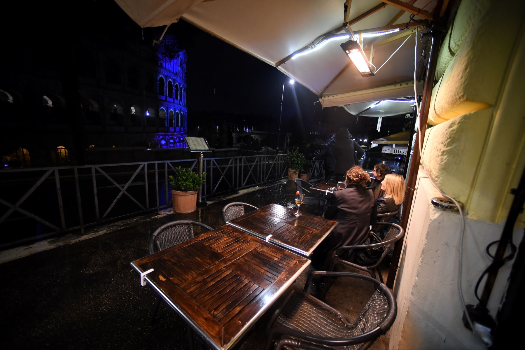 Las personas visitan restaurantes junto al coliseo que se ilumina por el 75 aniversario de la FAO, en el centro de Roma. Foto: AFP