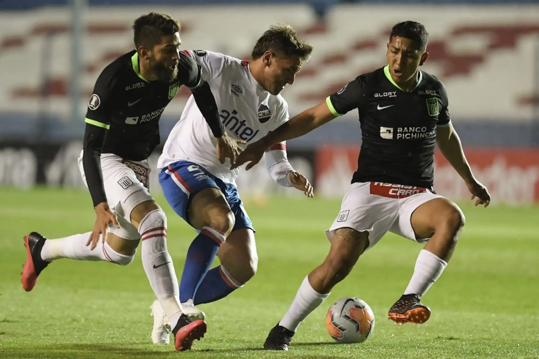 El delantero de la Nacional de Uruguay, el argentino Gonzalo Bergessio, compite por el balón con los peruanos Alianza Lima Rubert Quijada y Carlos Montoya durante su partido de fútbol a puerta cerrada en la fase de grupos de la Copa Libertadores en el Estadio Gran Parque Central de Montevideo. Foto: AFP
