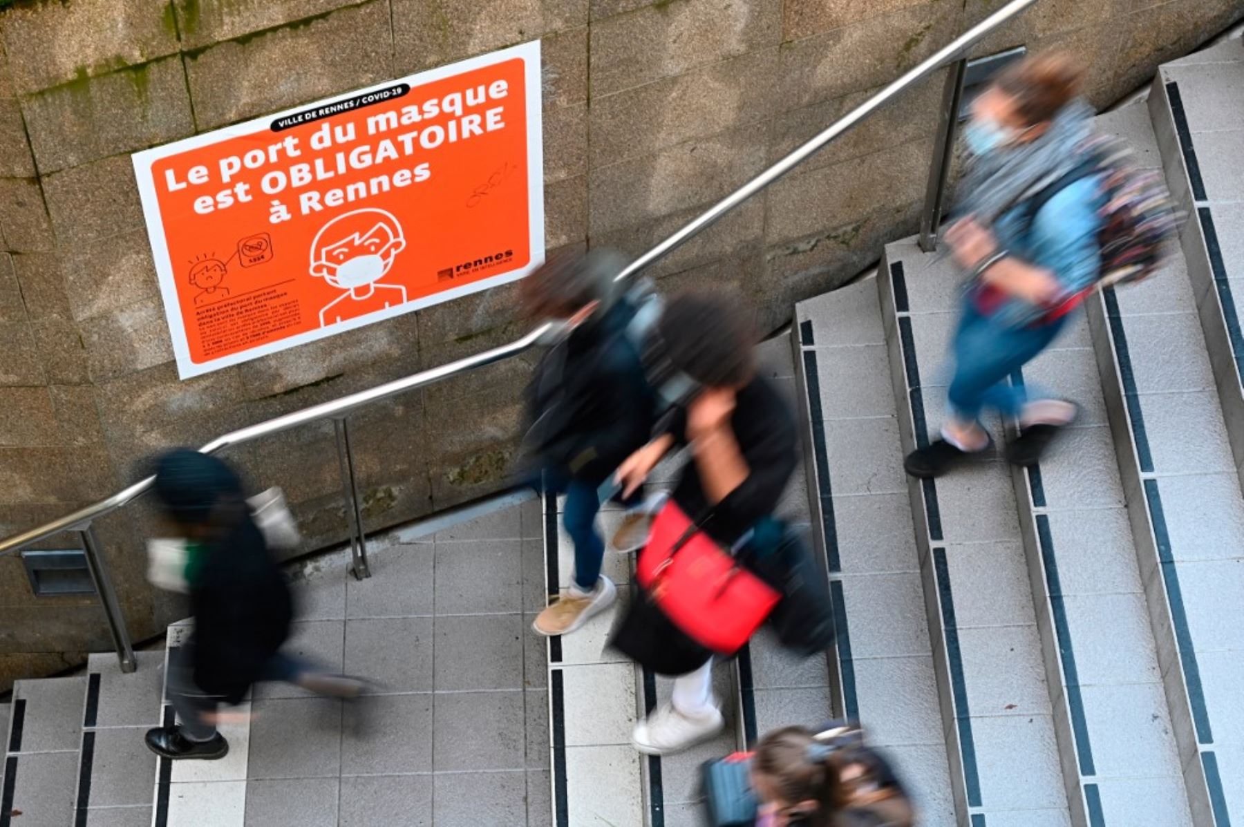 Personas que pasan junto a un letrero que dice "Es obligatorio llevar una máscara en Rennes" en la entrada del metro en Rennes, en el oeste de Francia. Foto: AFP