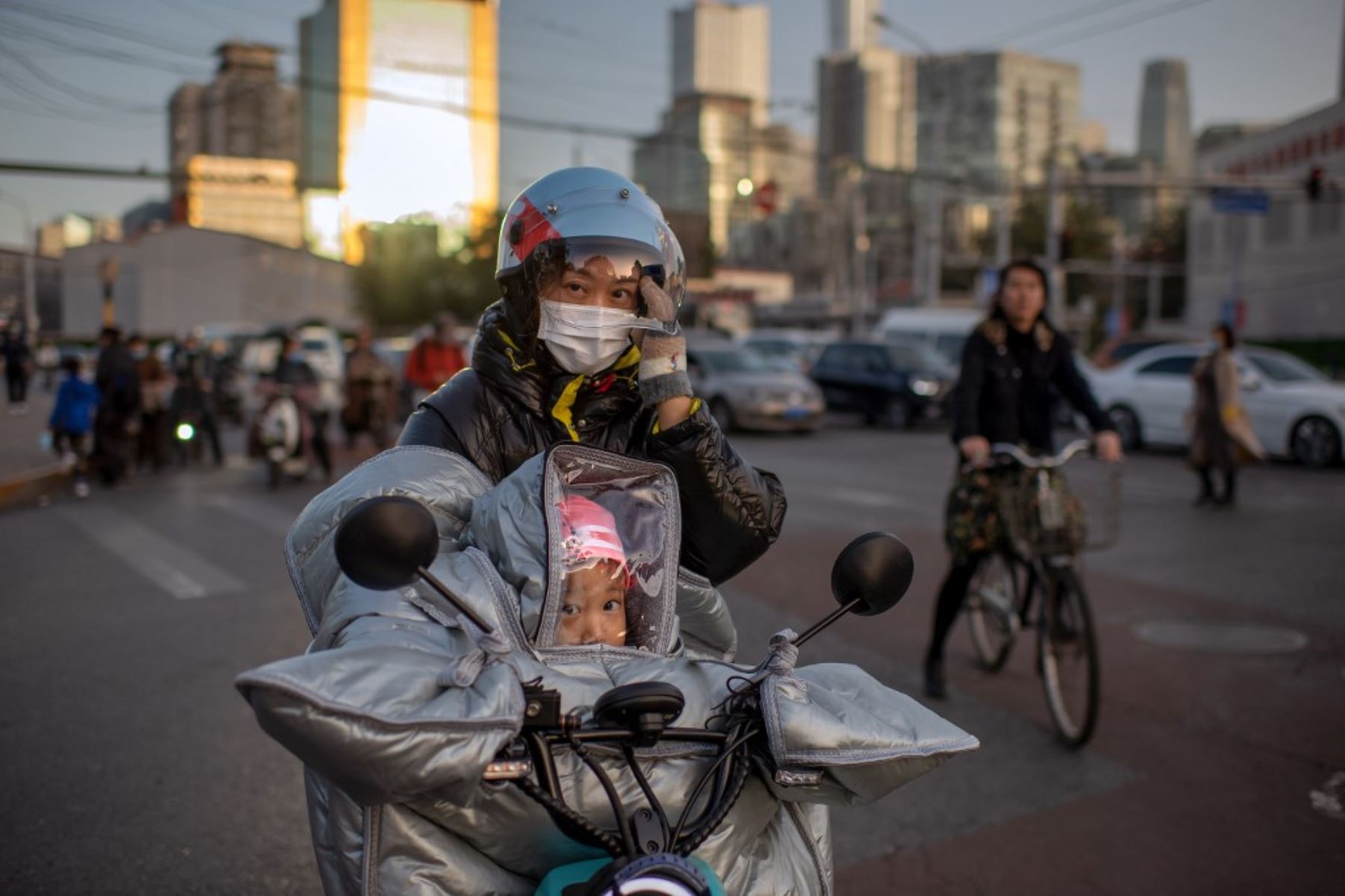 Una mujer que usa una mascarilla como medida preventiva contra el coronavirus covid-19 espera para cruzar una calle con su hija mientras ambas montan en una bicicleta eléctrica durante la hora pico en Beijing. Foto: AFP
