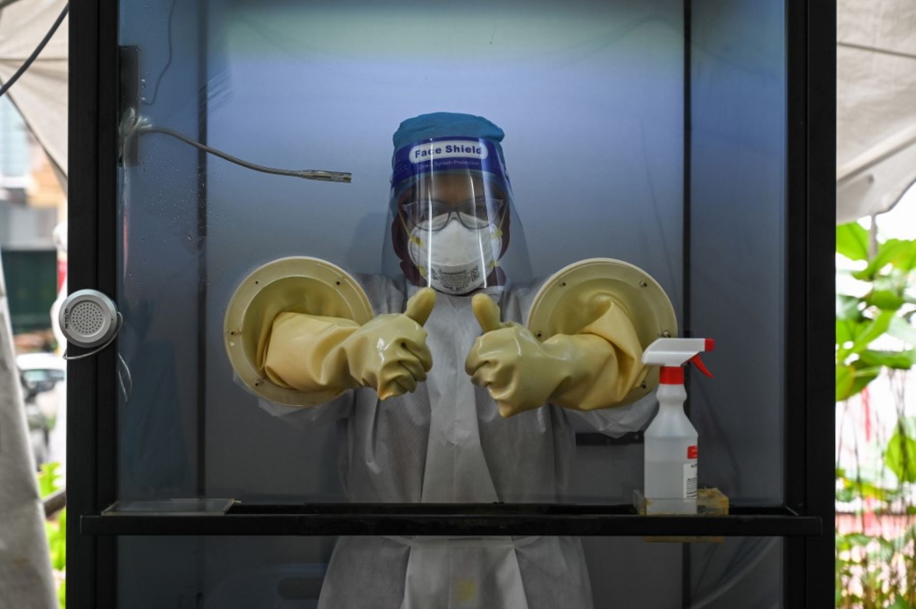 Una trabajadora de la salud levanta el pulgar mientras está de pie en una cámara sin contacto llamada "CoV SHIELD" antes de tomar hisopos para detectar el nuevo coronavirus covid-19 en el Sunway Medical Center en Subang Jaya, en las afueras de Kuala Lumpur. Foto: AFP