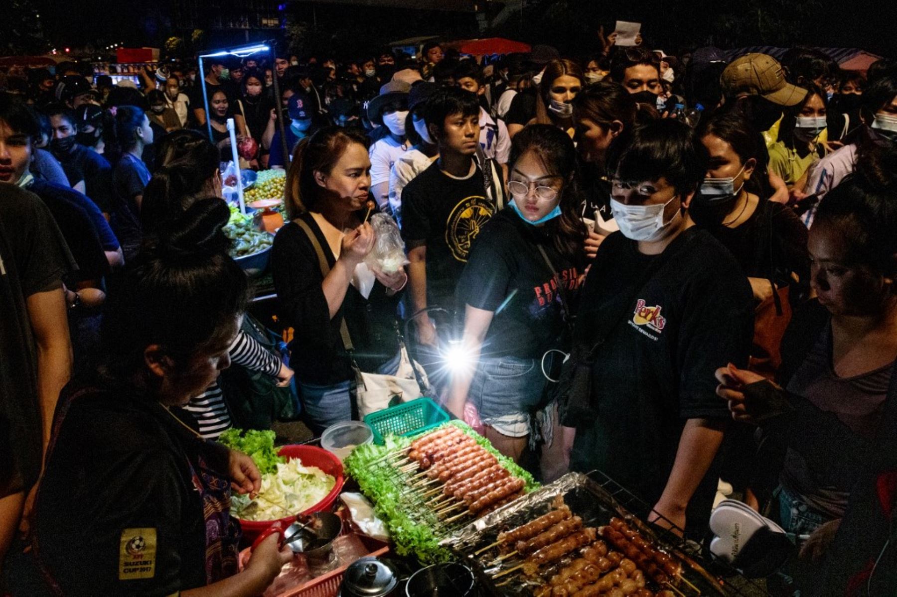 Manifestantes a favor de la democracia pasando junto a un vendedor ambulante de comida que vende salchichas a la parrilla durante una manifestación contra el gobierno en Bangkok. Foto: AFP