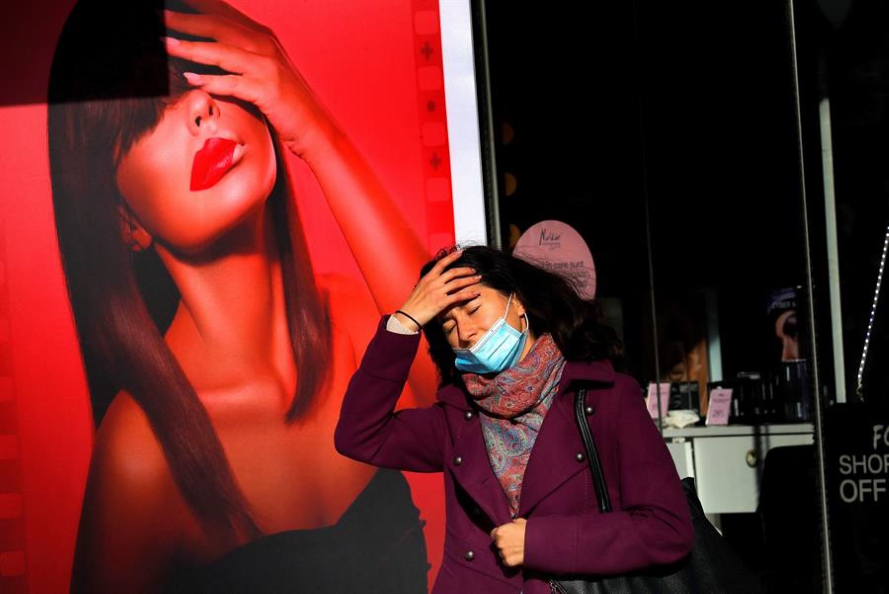 Una joven rumana con una máscara se arregla el cabello mientras pasa un anuncio de lápiz labial en el centro de Bucarest, Rumania. Debido al creciente número de infecciones por coronavirus, las autoridades han implementado el 