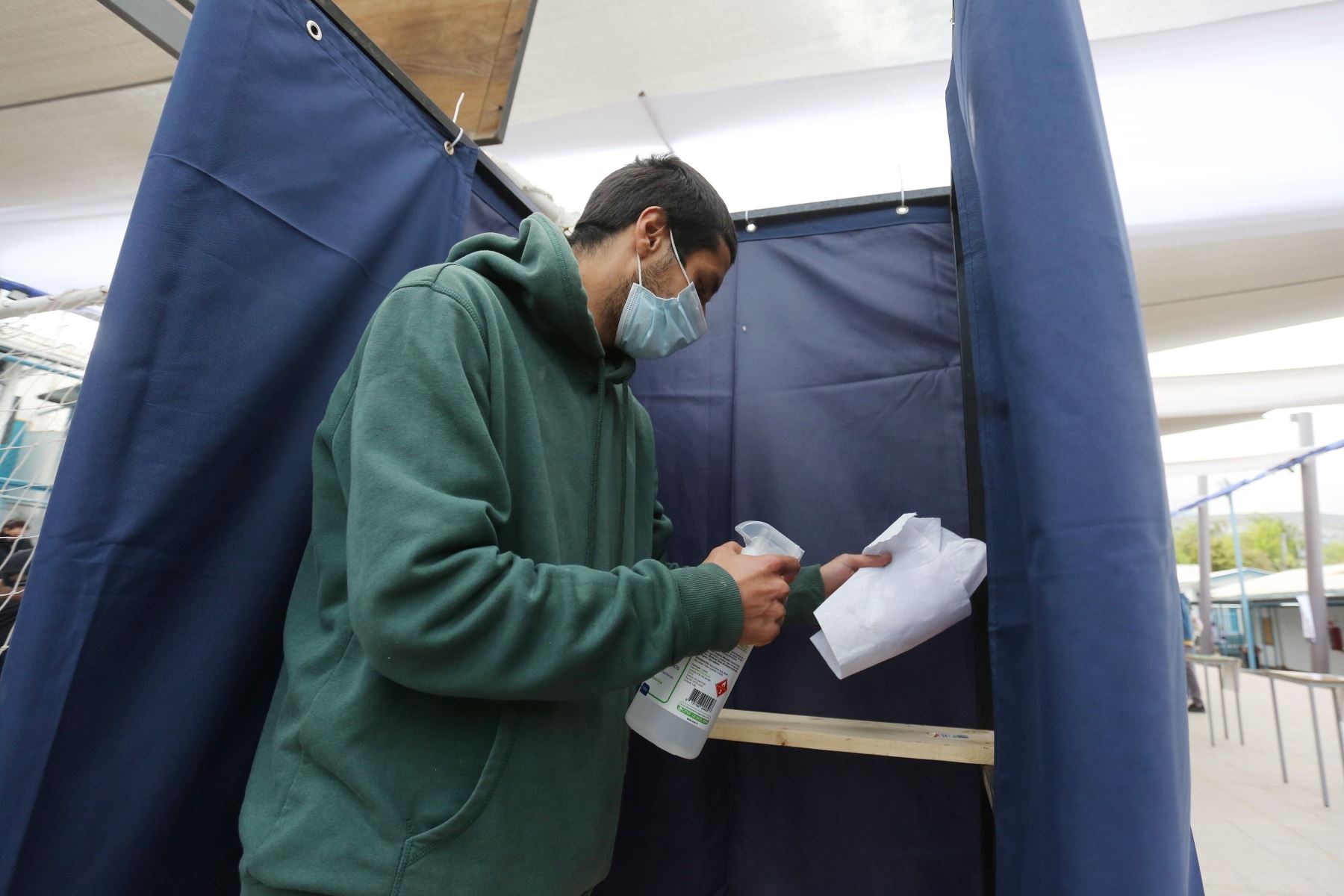Un hombre desinfecta una cabina de votación en un colegio electoral, este domingo, en Santiago de Chile. Foto: EFE