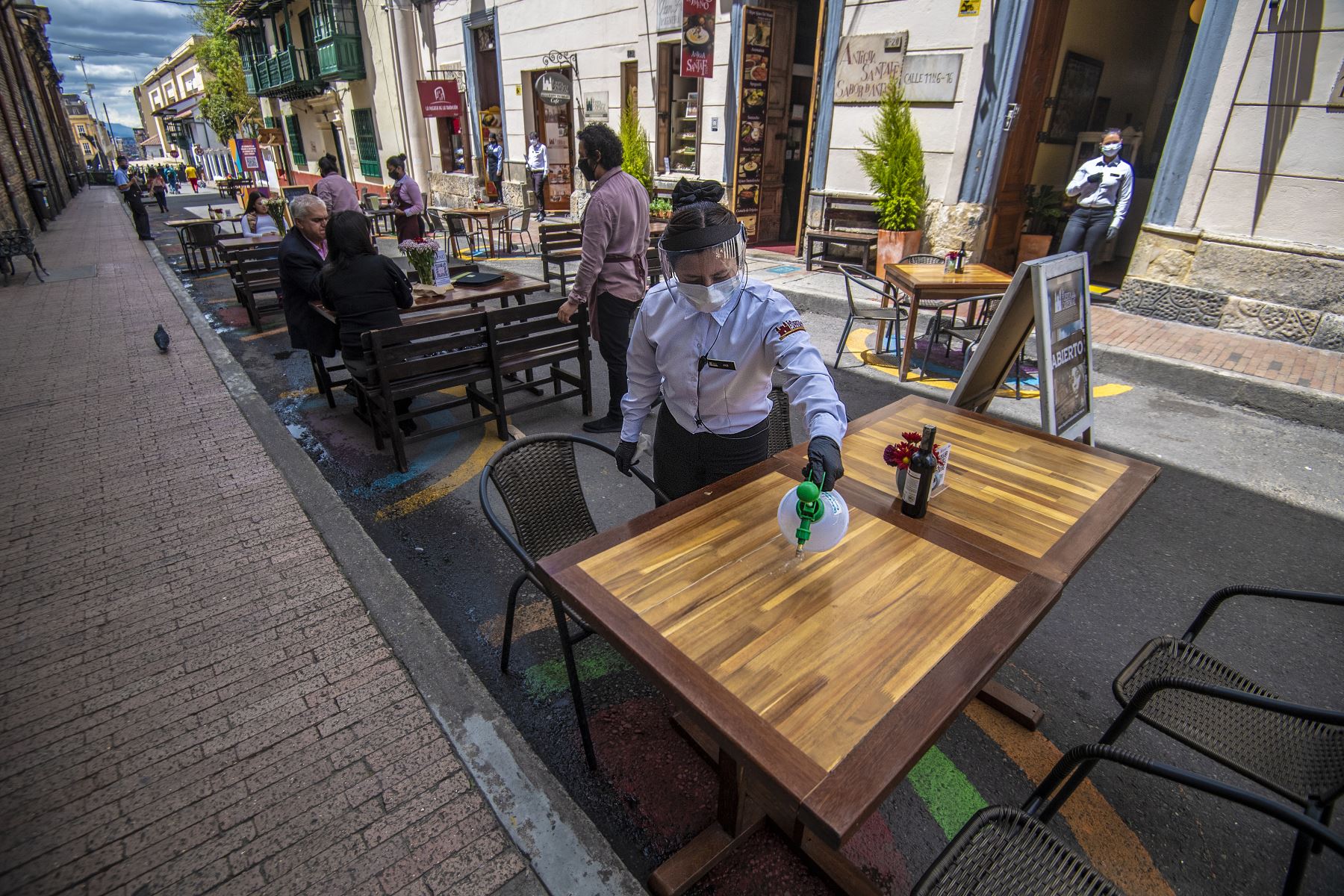 Un servidor con mascarilla y protector facial limpia una mesa en un restaurante en Bogotá. Foto: AFP