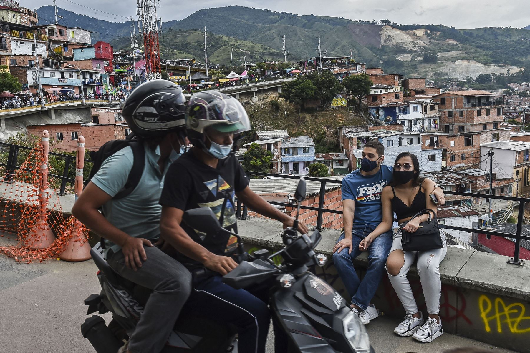 Una motocicleta pasa frente a una pareja sentada en el barrio Comuna 13 mientras el sector turístico se reactiva en Medellín, Colombia. Foto: AFP