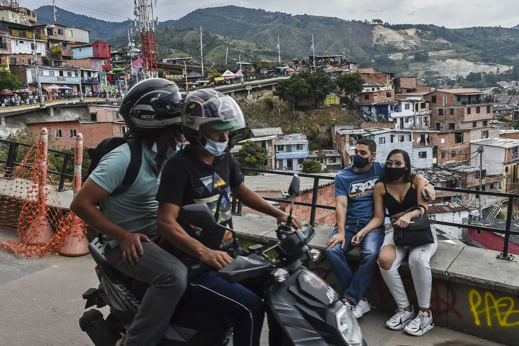 Una motocicleta pasa frente a una pareja sentada en el barrio Comuna 13 mientras el sector turístico se reactiva en Medellín, Colombia. Foto: AFP