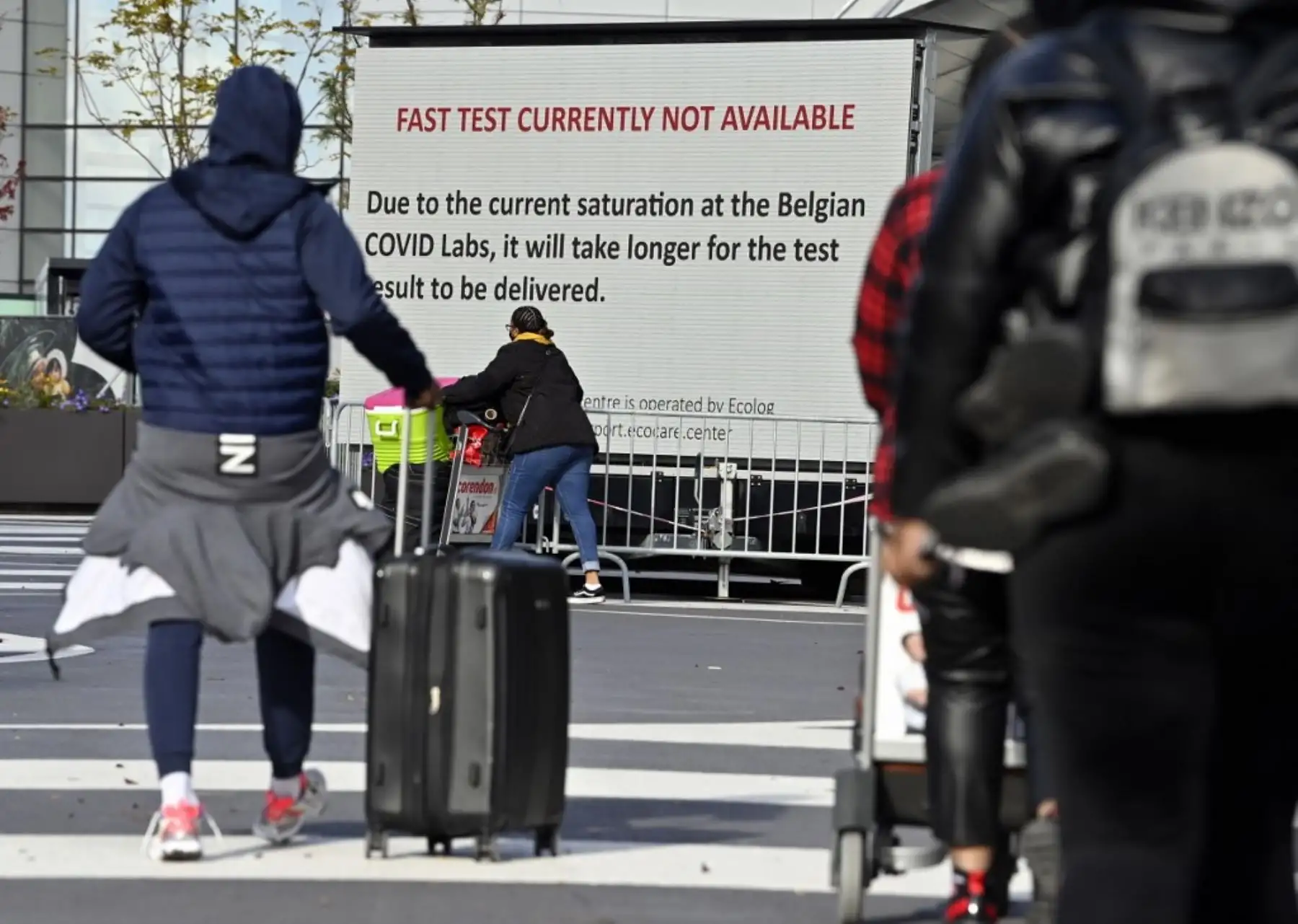Personas hacen cola junto a un panel de información cerca de una estación de pruebas instalada para Covid-19 en el aeropuerto de Bruselas, en Zaventem. Foto: AFP