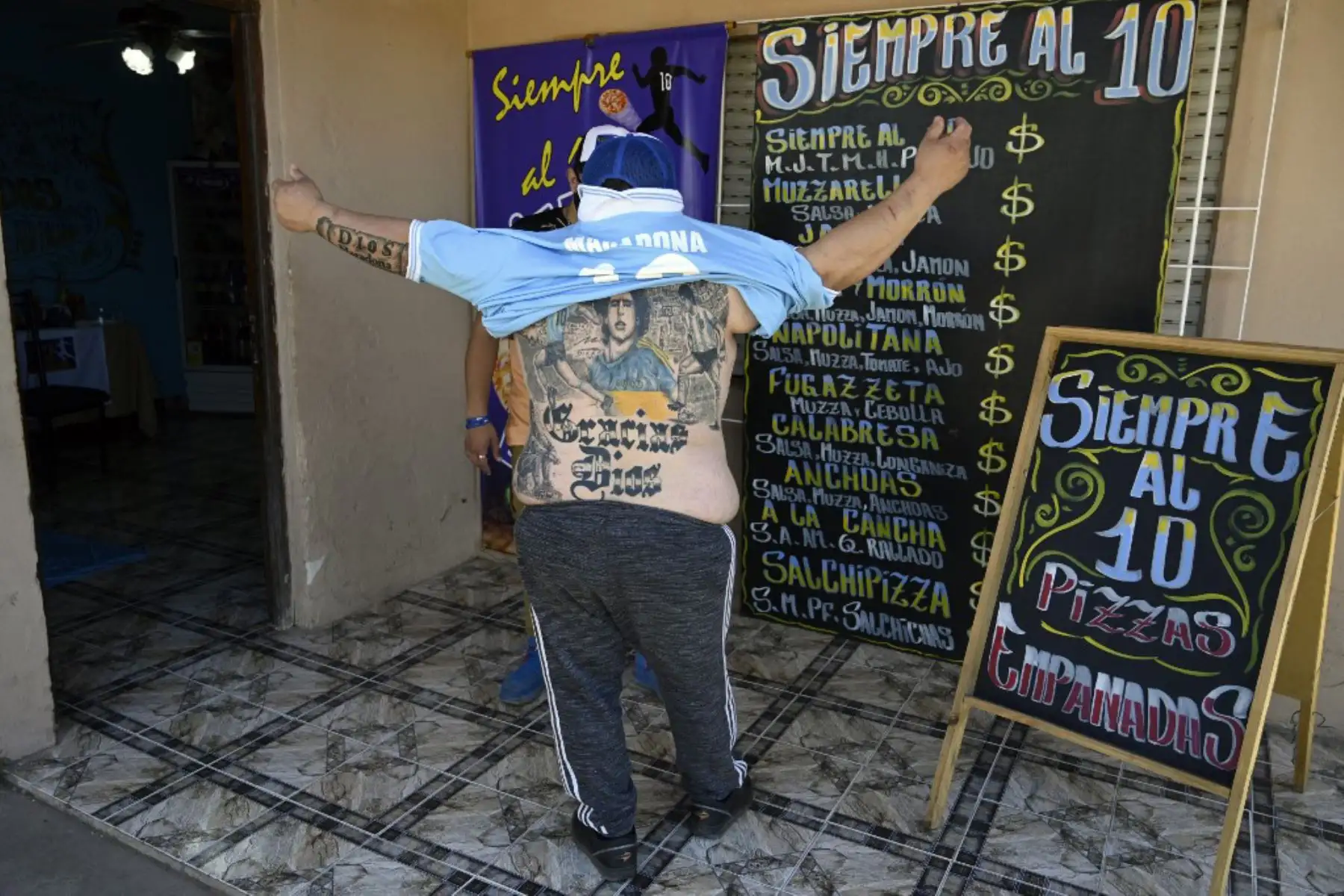 El pizzero Guillermo Rodríguez, bautizado en la iglesia Maradoniana, muestra los tatuajes en su espalda que representan a la leyenda del fútbol argentino Diego Maradona, en su pizzería llamada "Siempre al 10" (Siempre al 10), en referencia al número de la ex camiseta de su ídolo. , en Merlo, provincia de Buenos Aires. Rodríguez se hizo este tatuaje para conmemorar el 60 cumpleaños del actual entrenador de Gimnasia y Esgrima, que será el próximo 30 de octubre.

Foto: AFP