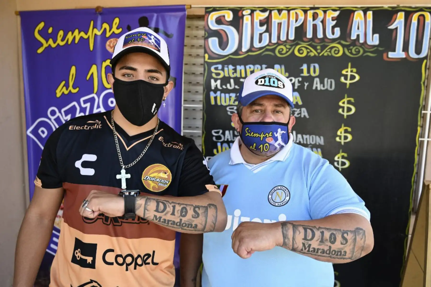 El pizzero Guillermo Rodríguez (derecha) y su hijo Axel, ambos bautizados en la iglesia de Maradonian, muestran los tatuajes en sus brazos que dicen "Dios Maradona", en referencia a la leyenda del fútbol argentino Diego Maradona, en su pizzería llamada "Siempre al 10", Argentina. Rodríguez se hizo este tatuaje para conmemorar al actual entrenador del 60 cumpleaños de Gimnasia y Esgrima, que será el próximo 30 de octubre

Foto: AFP