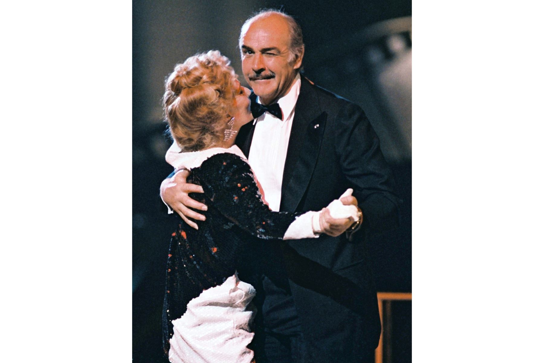 El actor escocés Sean Connery guiña un ojo al fotógrafo mientras baila junto a la actriz francesa Jeanne Moreau, el 07 de marzo de 1987, durante la ceremonia anual de premios de la industria cinematográfica francesa, en París. Foto: AFP