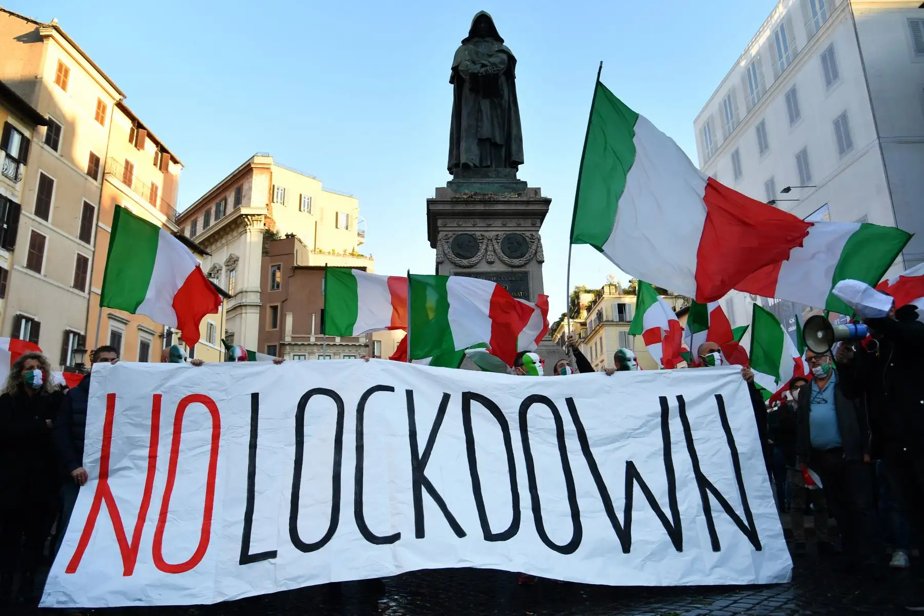 Manifestantes con máscaras protestan ante nuevas restricciones. Llevan una pancartas y flamean su bandera, en Roma, Italia. Foto: AFP