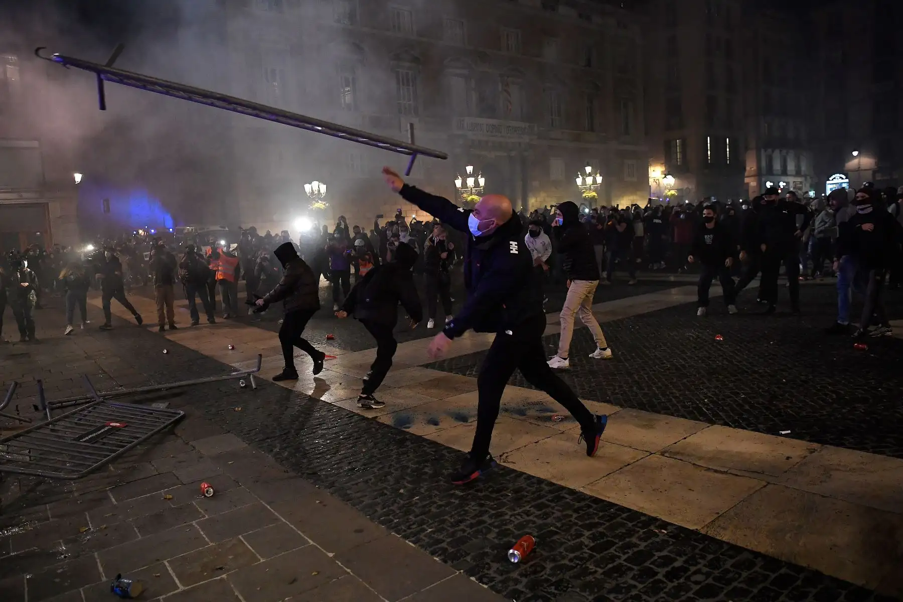 Los manifestantes lanzan barreras de control hacia los miembros de la Policía regional catalana durante una manifestación contra las nuevas restricciones del coronavirus, en Barcelona. Foto: AFP