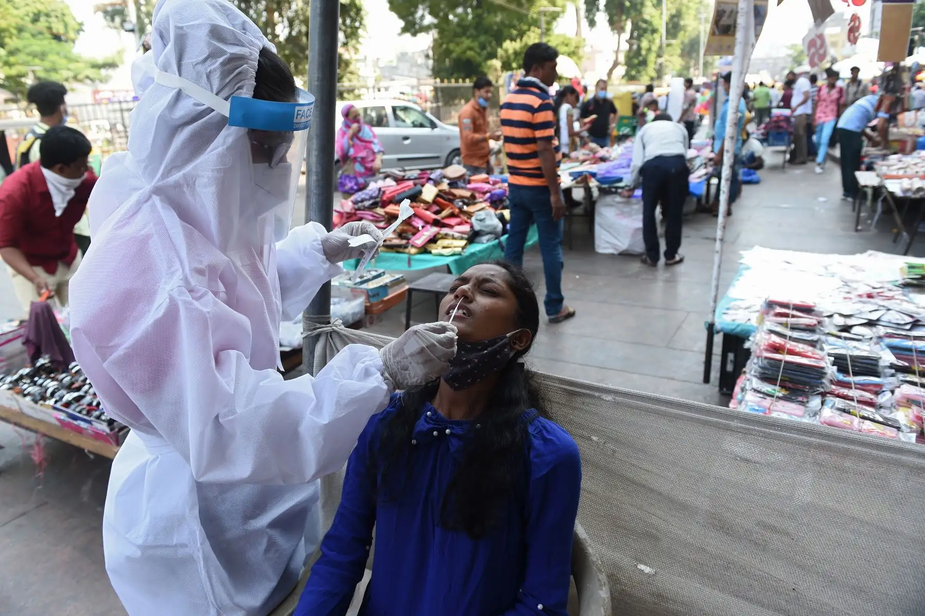 Un trabajador de la salud recolecta una muestra de hisopo de una mujer para realizar la prueba del coronavirus, en un mercado en Ahmedabad, en la India. Foto: AFP