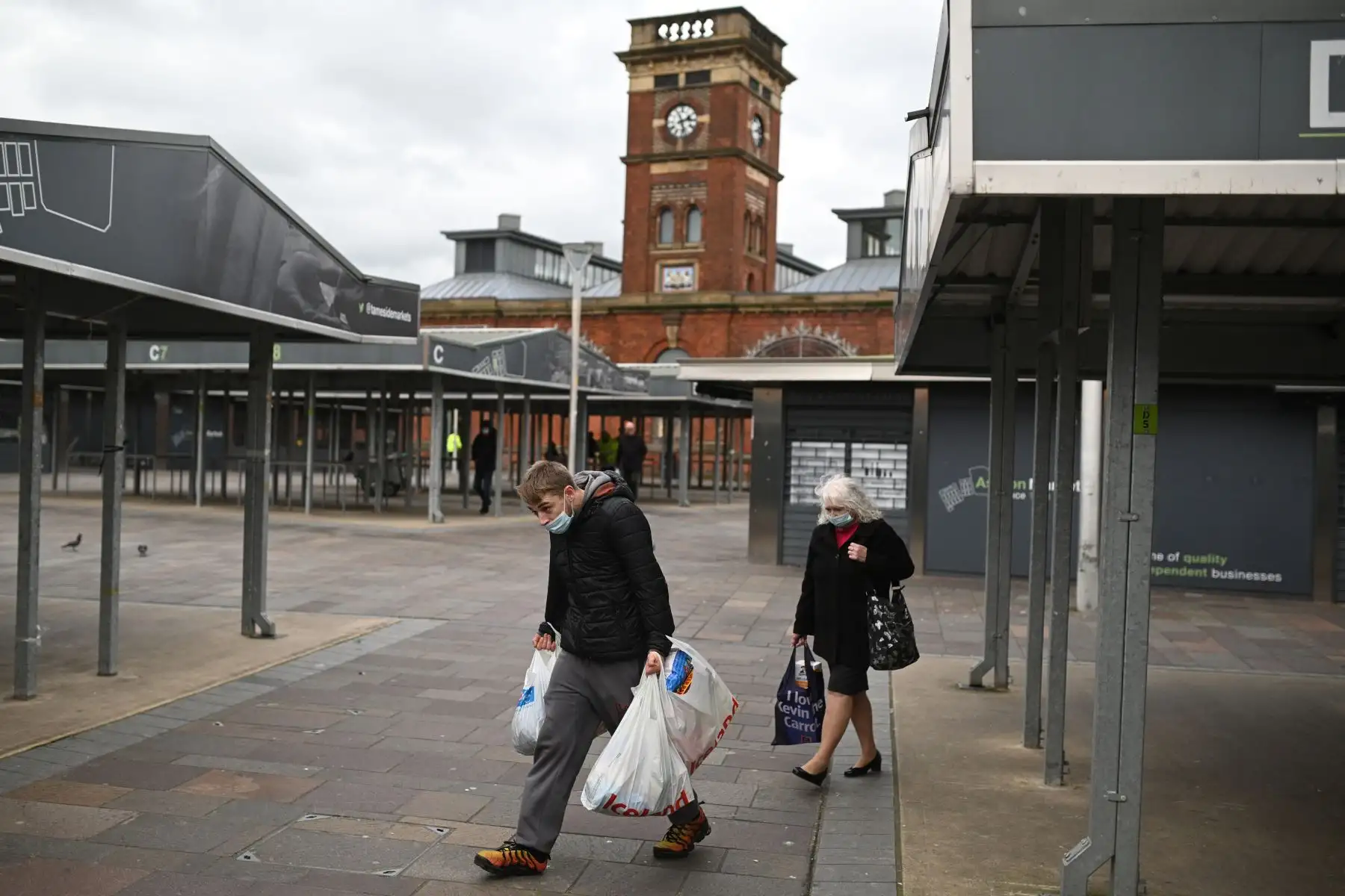 Las personas llevan protectores faciales mientras caminan por un mercado desierto en Ashton-under-Lyne, al este de Manchester, en el noroeste de Inglaterra. Foto: AFP