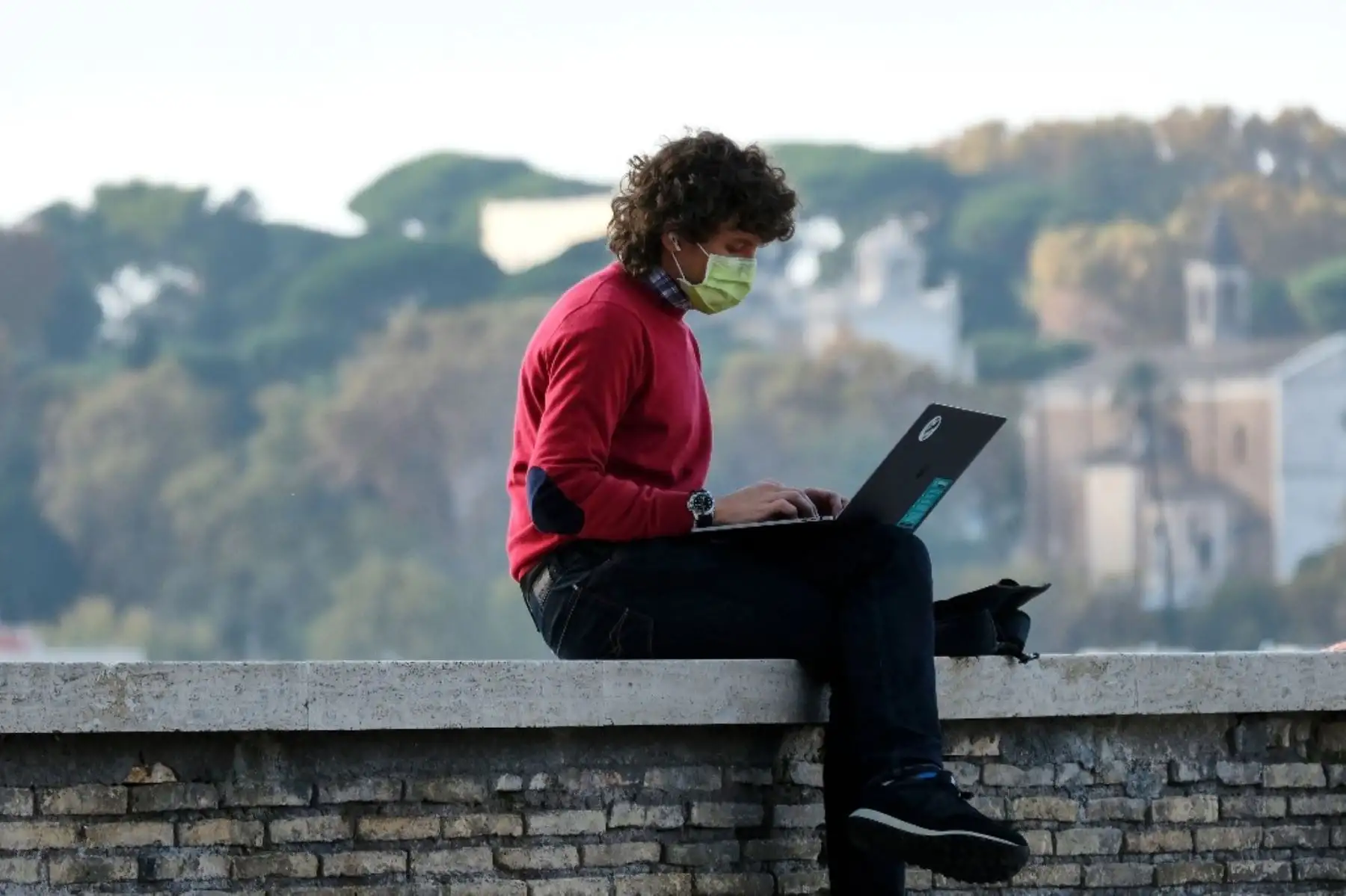 Un hombre con una máscara quirúrgica protectora trabaja en su computadora portátil en una terraza de los Jardines de Naranjas (Giardino degli Aranci) en la Colina Aventina en Roma. Foto: AFP