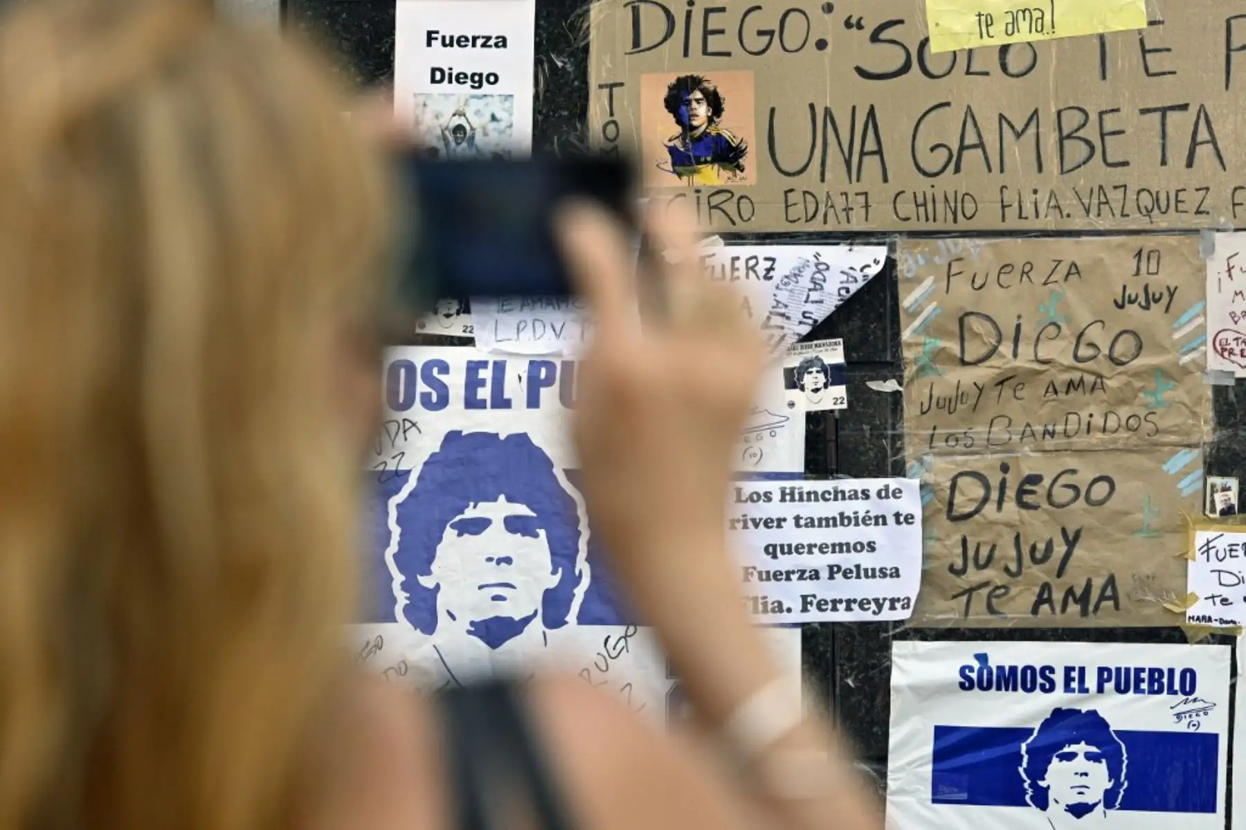 Una mujer toma una foto de los mensajes de apoyo colocados fuera de la clínica privada donde la ex estrella del fútbol argentino y entrenador de Gimnasia y Esgrima La Plata Diego Maradona se sometió a una cirugía cerebral por un coágulo de sangre, en Olivos, provincia de Buenos Aires. Foto: AFP