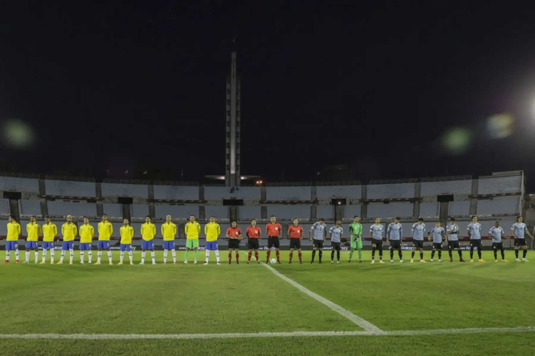 Jugadores de Brasil (izq.) y Uruguay escuchan los himnos nacionales antes de su partido a puertas cerradas clasificatorio sudamericano para la Copa Mundial de la FIFA 2022 en el Estadio Centenario de Montevideo. Foto: AFP