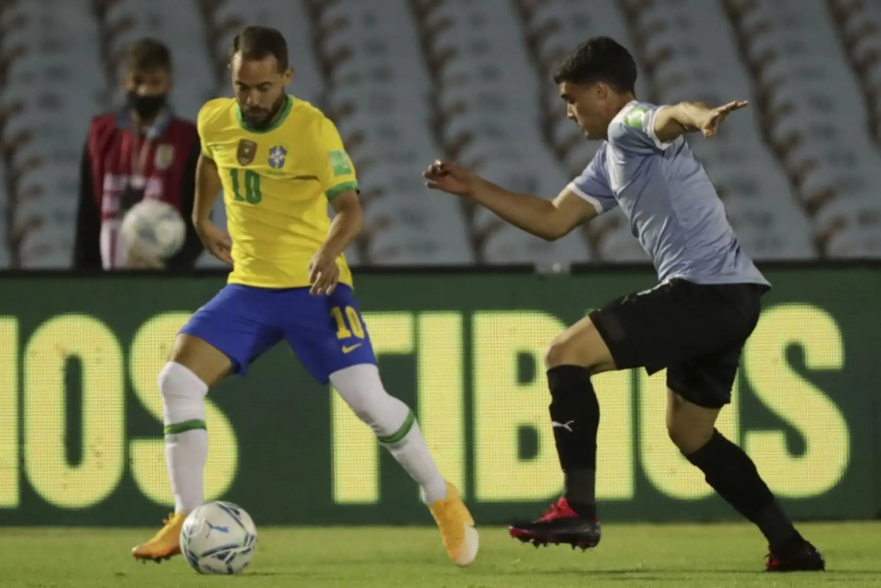 El brasileño Everton Ribeiro (izq.) Y el uruguayo Agustín Oliveros compiten por el balón durante su partido de fútbol a puertas cerradas clasificatorio sudamericano para la Copa Mundial de la FIFA 2022 en el Estadio Centenario de Montevideo. Foto: AFP