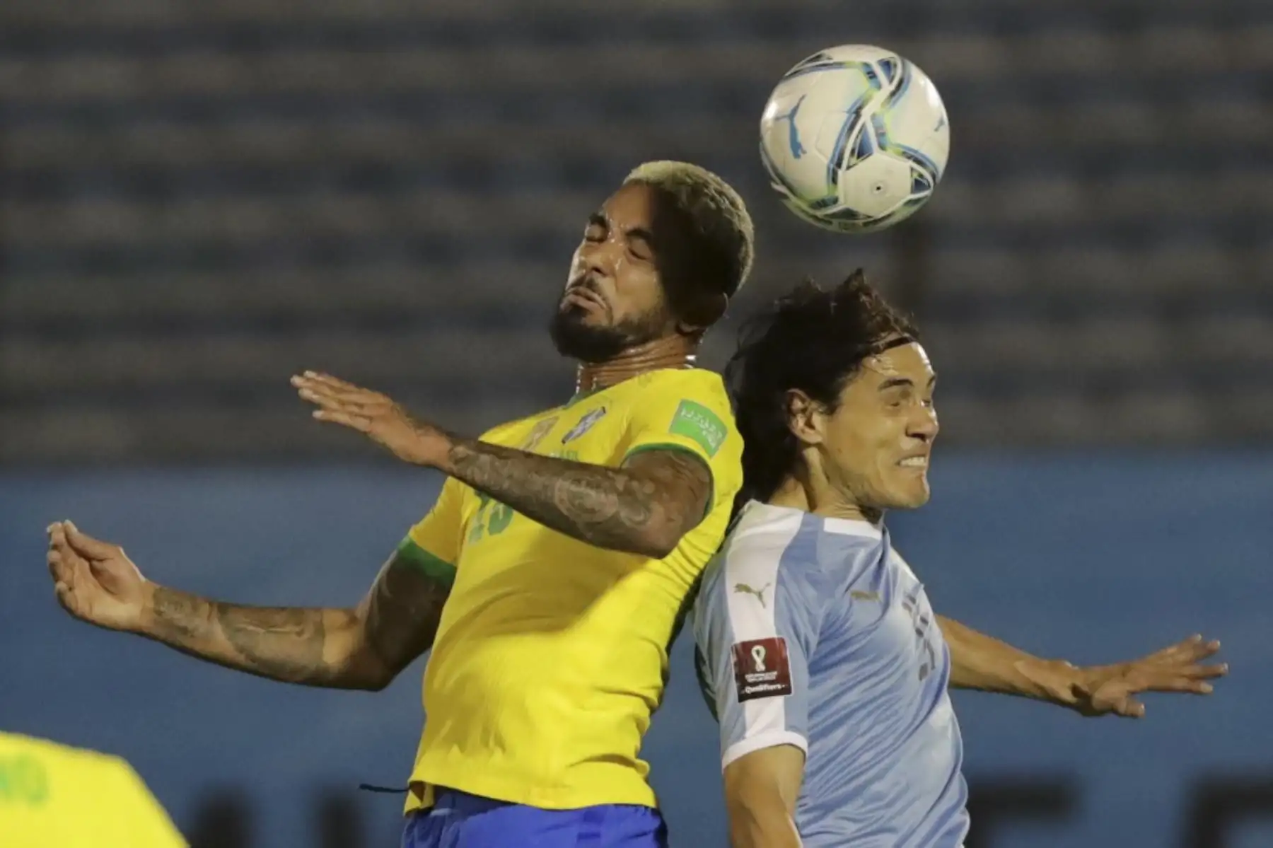 El brasileño Douglas Luiz (izq.) Y el uruguayo Edinson Cavani saltan de cabeza durante su partido de fútbol a puertas cerradas clasificatorio sudamericano para la Copa Mundial de la FIFA 2022 en el Estadio Centenario de Montevideo. Foto: AFP