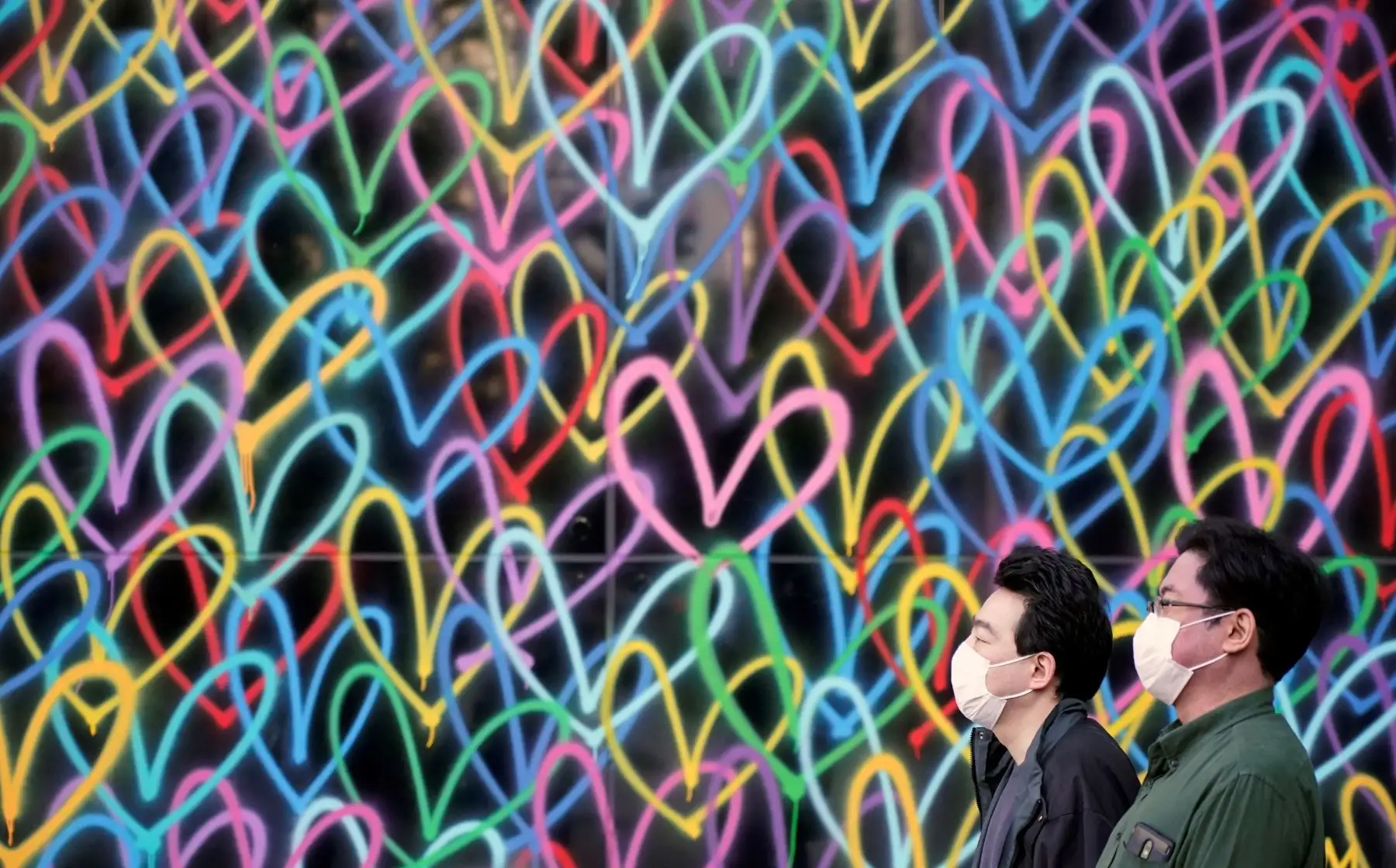 Los transeúntes con mascarillas pasan ante una pared pintada en un distrito de negocios en Tokio. Foto: EFE