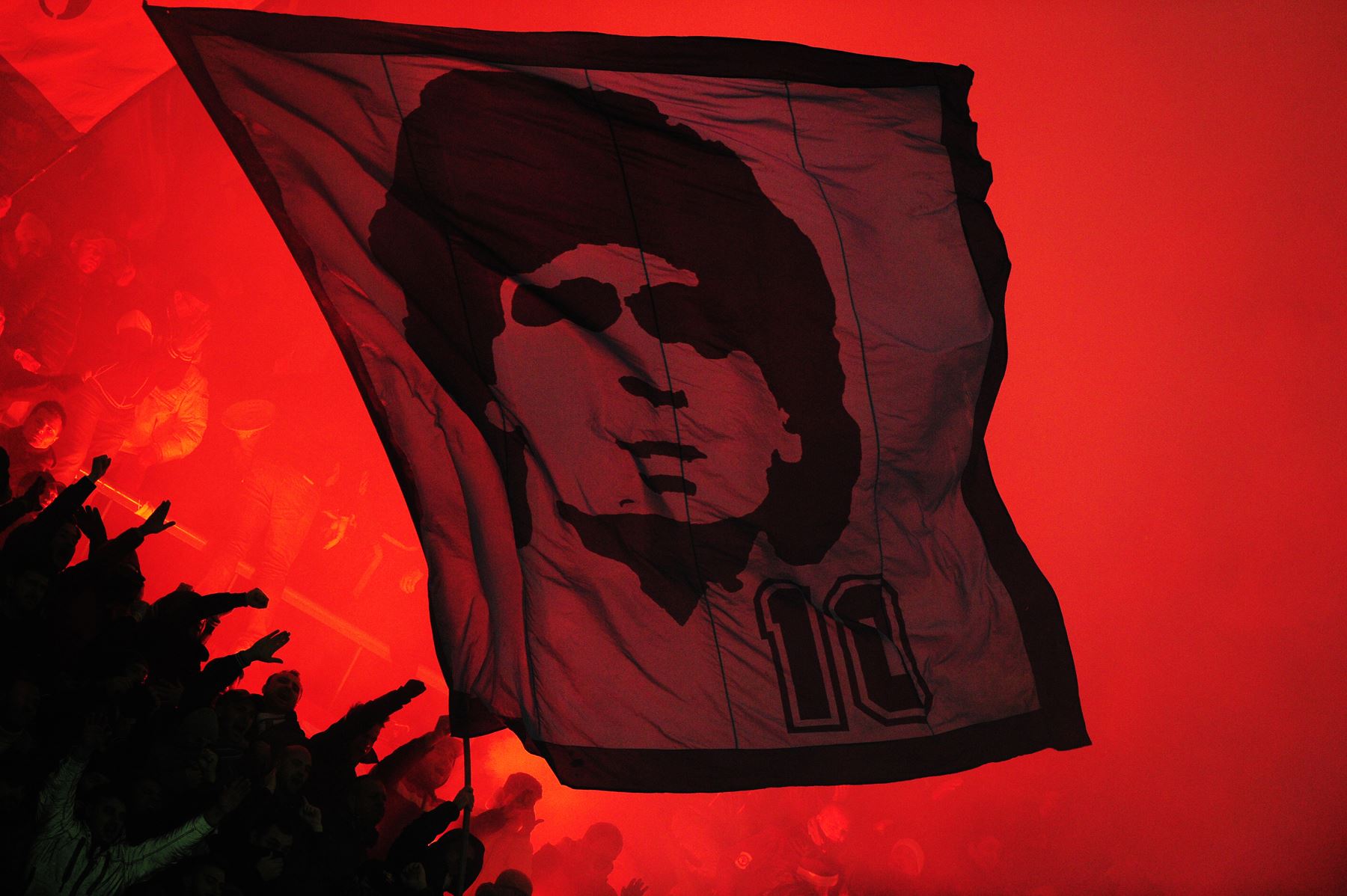 En esta foto de archivo tomada el 15 de diciembre de 2013, los seguidores del SSC Napoli ondean una bandera con un retrato de la leyenda del fútbol argentino Diego Maradona durante el partido de fútbol de la Serie A SSC Napoli vs Inter de Milán en el estadio San Paolo de Nápoles. Foto: AFP
