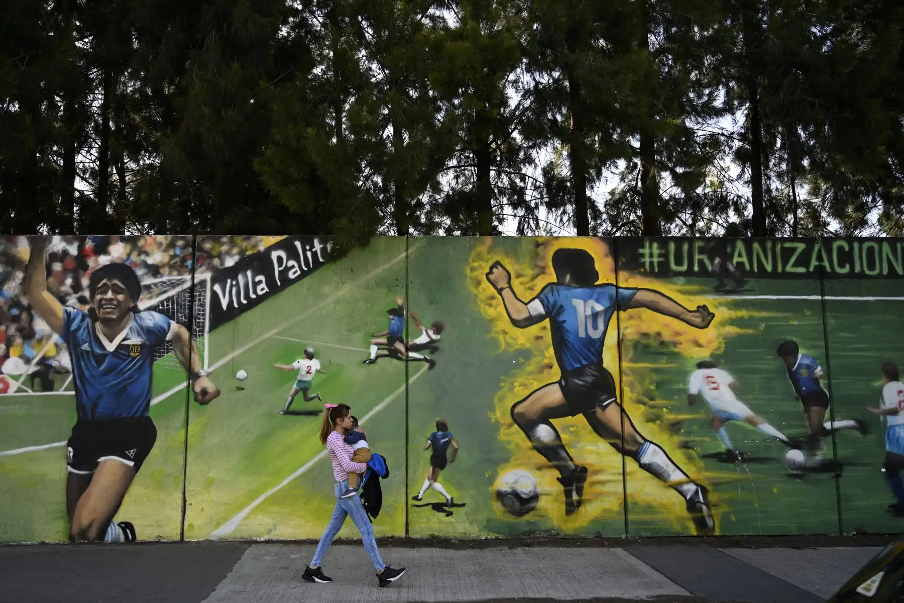 Una mujer pasa junto a un mural del artista callejero "Uasen" que representa al ex astro del fútbol argentino Diego Maradona, actual entrenador de la selección Gimnasia y Esgrima La Plata, anotando el segundo gol en el partido de la Copa Mundial de la FIFA México 86 contra Inglaterra, en Villa Palito. Foto: AFP