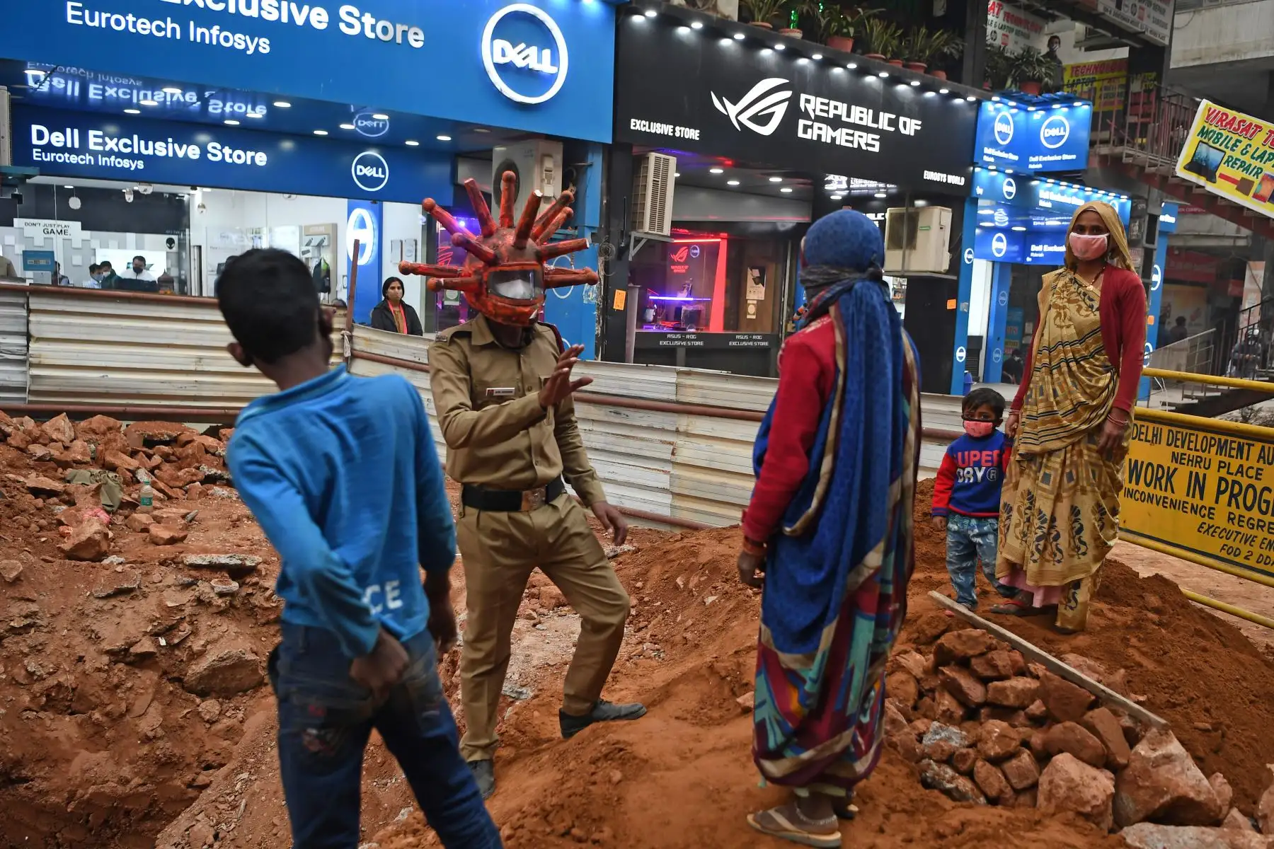 Un voluntario de defensa civil que lleva un casco que hace referencia al Covid-19 habla con trabajadores durante una campaña de concientización en un mercado en Nueva Delhi, India. Foto: AFP