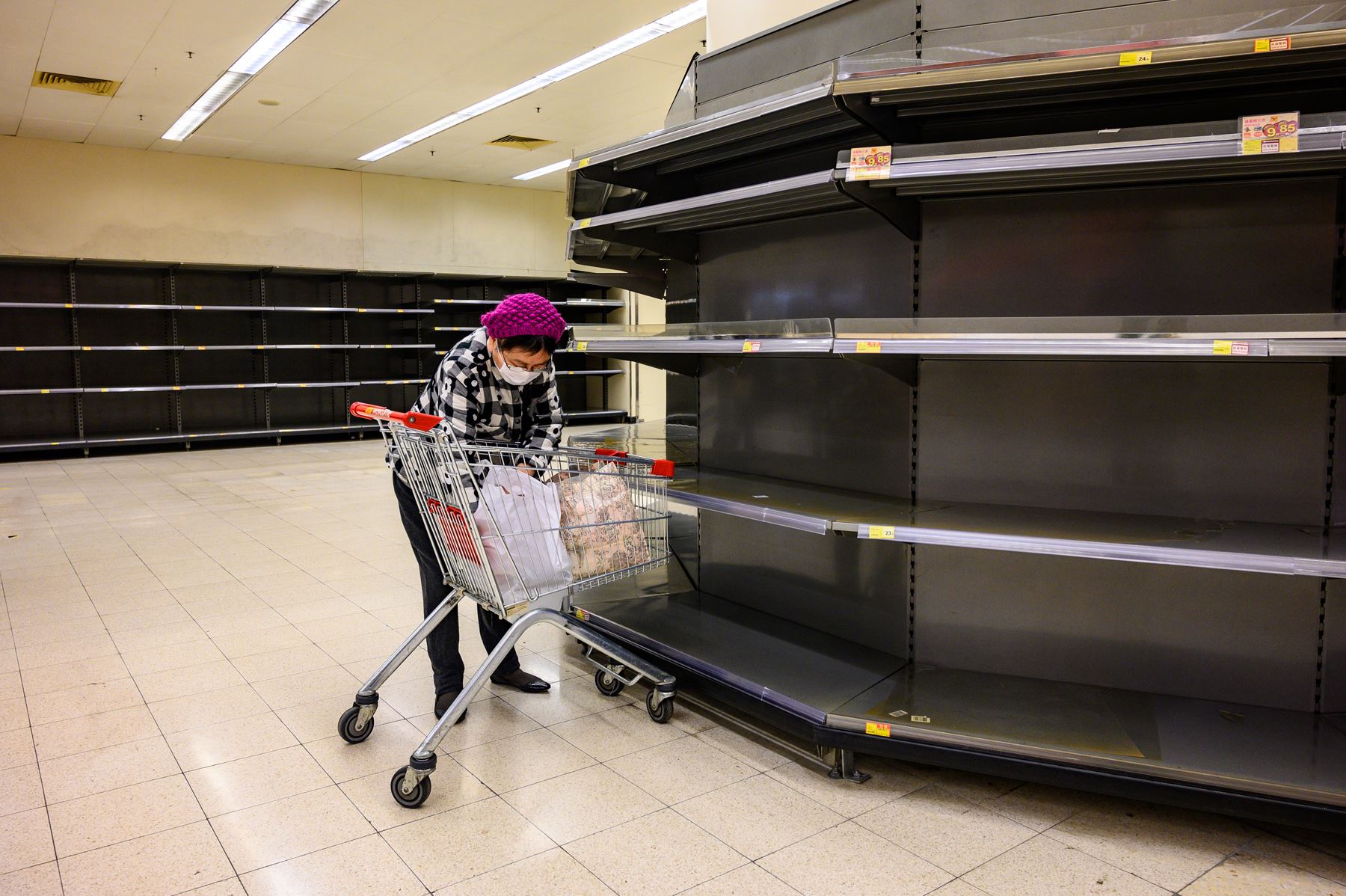 Una mujer que lleva una mascarilla protectora clasifica los artículos en su carrito mientras se observa los estantes vacíos del supermercado. Foto: AFP