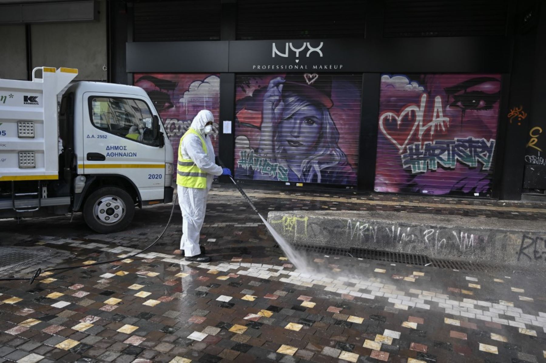 Un trabajador municipal desinfecta cerca de tiendas cerradas en el centro de Atenas. Foto: AFP