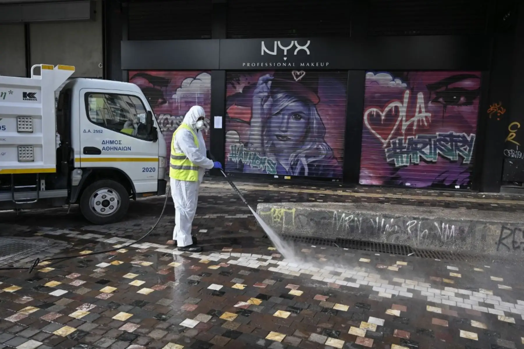 Un trabajador municipal desinfecta cerca de tiendas cerradas en el centro de Atenas. Foto: AFP