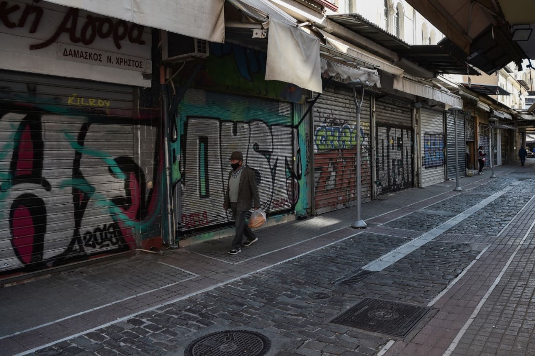 Un hombre que llevaba una mascarilla pasa junto a los lúpulos cerrados en Salónica durante un segundo cierre nacional en Grecia destinado a frenar la propagación de la pandemia Covid-19, causada por el nuevo coronavirus. Foto: AFP
