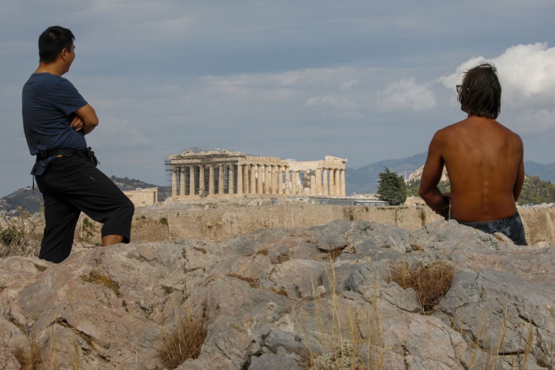 Turistas se sientan bajo el sol en una colina con vistas a la antigua Acrópolis del siglo V A.C, en Atenas. La industria del turismo en Grecia se ha visto muy afectada durante la pandemia del nuevo coronavirus covid-19. Foto: AFP