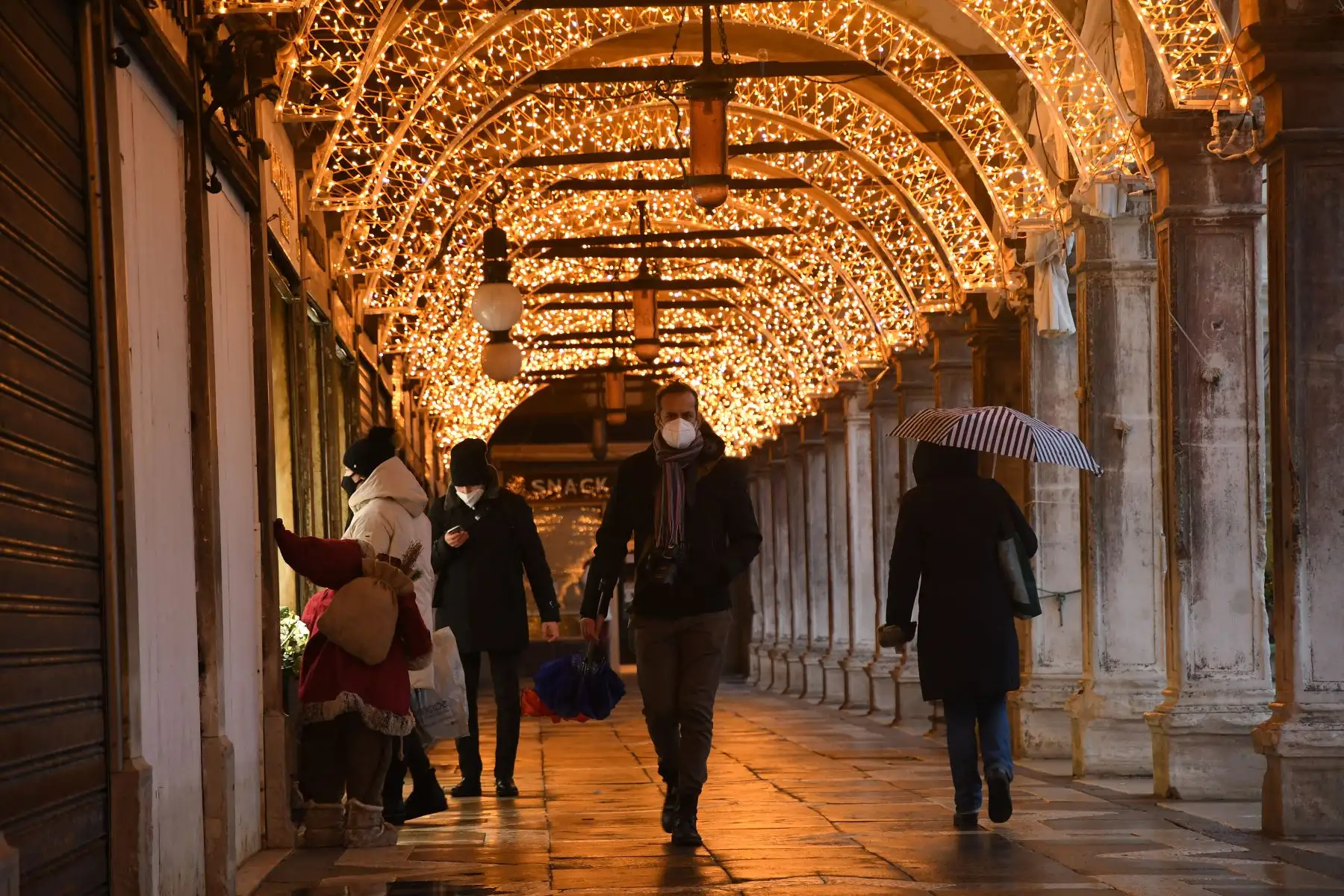 Personas caminando bajo las decoraciones navideñas instaladas en una galería comercial desierta junto a la Plaza de San Marcos, durante las medidas de restricción del gobierno para frenar la propagación de la pandemia, en Venecia. Foto: AFP