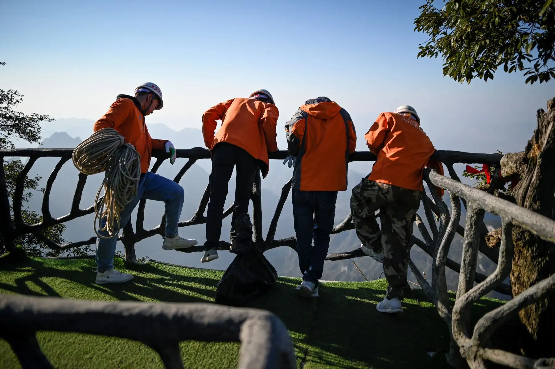 Un grupo de limpiadores observan a su compañero mientras recolecta basura en la montaña Tianmen, en Zhangjiajie, China. Foto: AFP